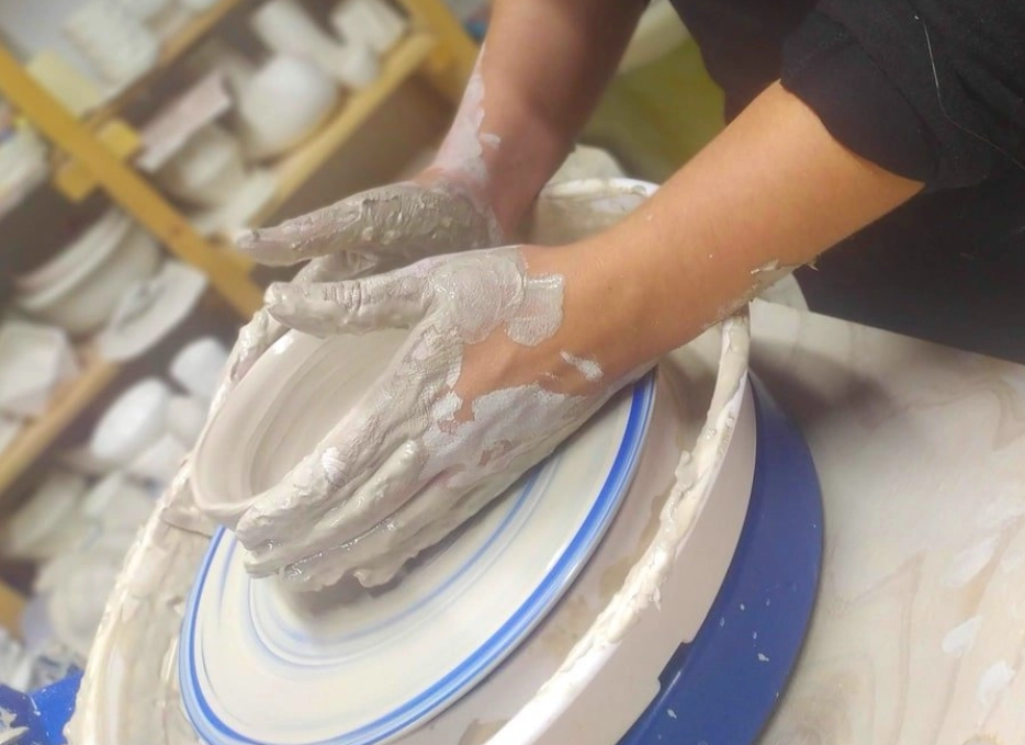 Person shaping clay on a pottery wheel with their hands covered in wet clay.