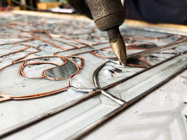 Close-up of a welding process on metal, with a welding torch and heated metal wires forming a design for a stained glass panel.