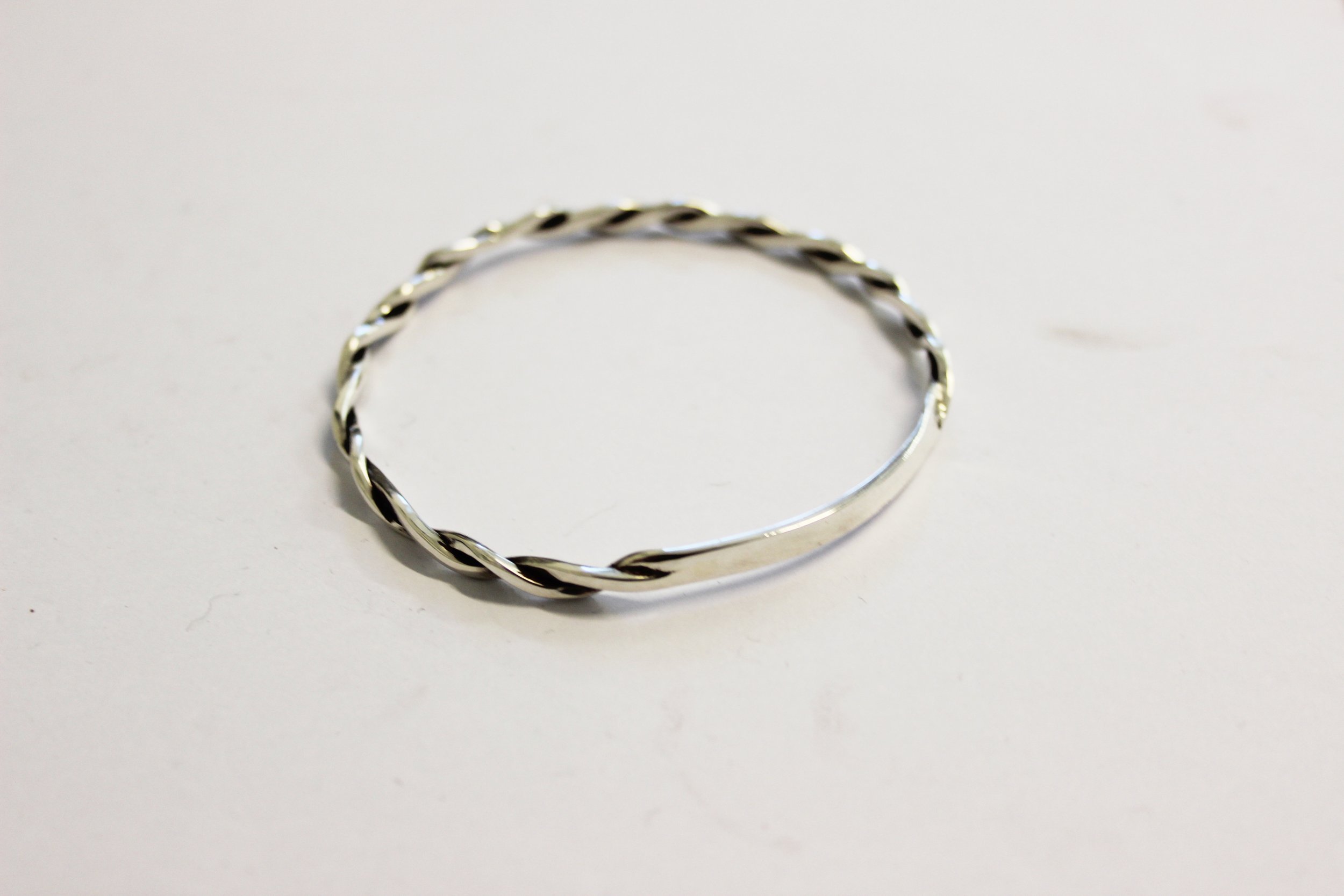 Handmade silver twisted bracelet on a white surface.