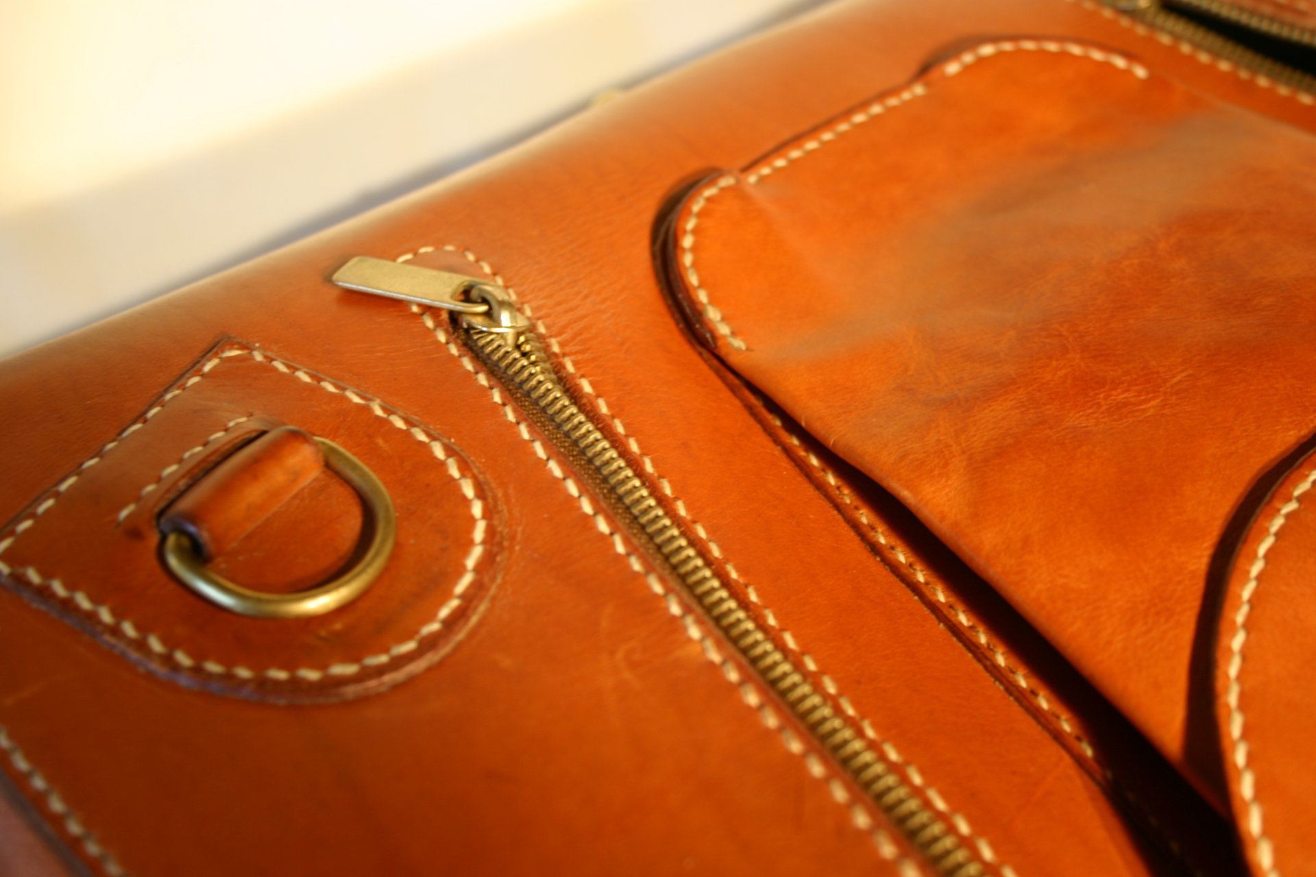 Close-up of an orange leather bag with a zipper, a D-ring, and a small pocket, with white stitching details.
