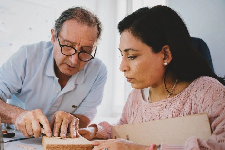 Artisan demonstrating leatherworking techniques to a woman in a hands-on workshop.