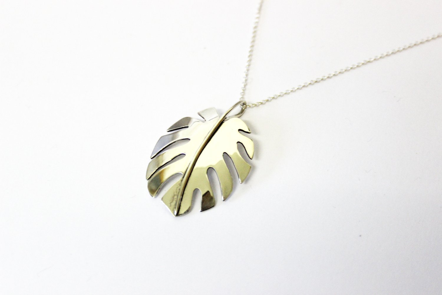 Silver necklace with a pendant shaped like a Monstera leaf.