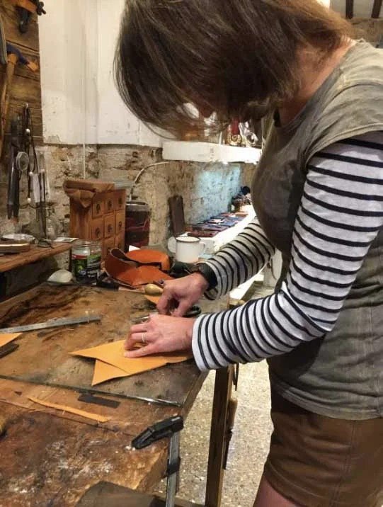 Woman in striped shirt working on two pieces of leather during a workshop in Barcelona.
