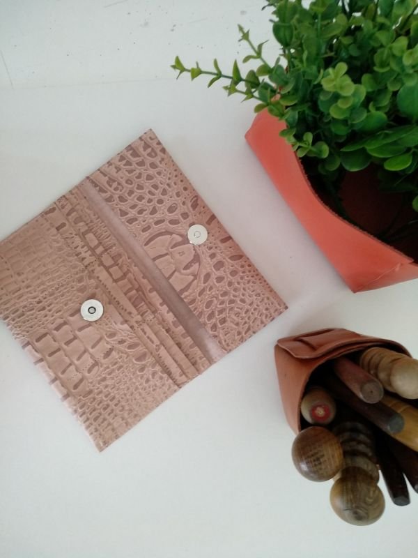 Open leather wallet next to a plant and leatherworking tools.