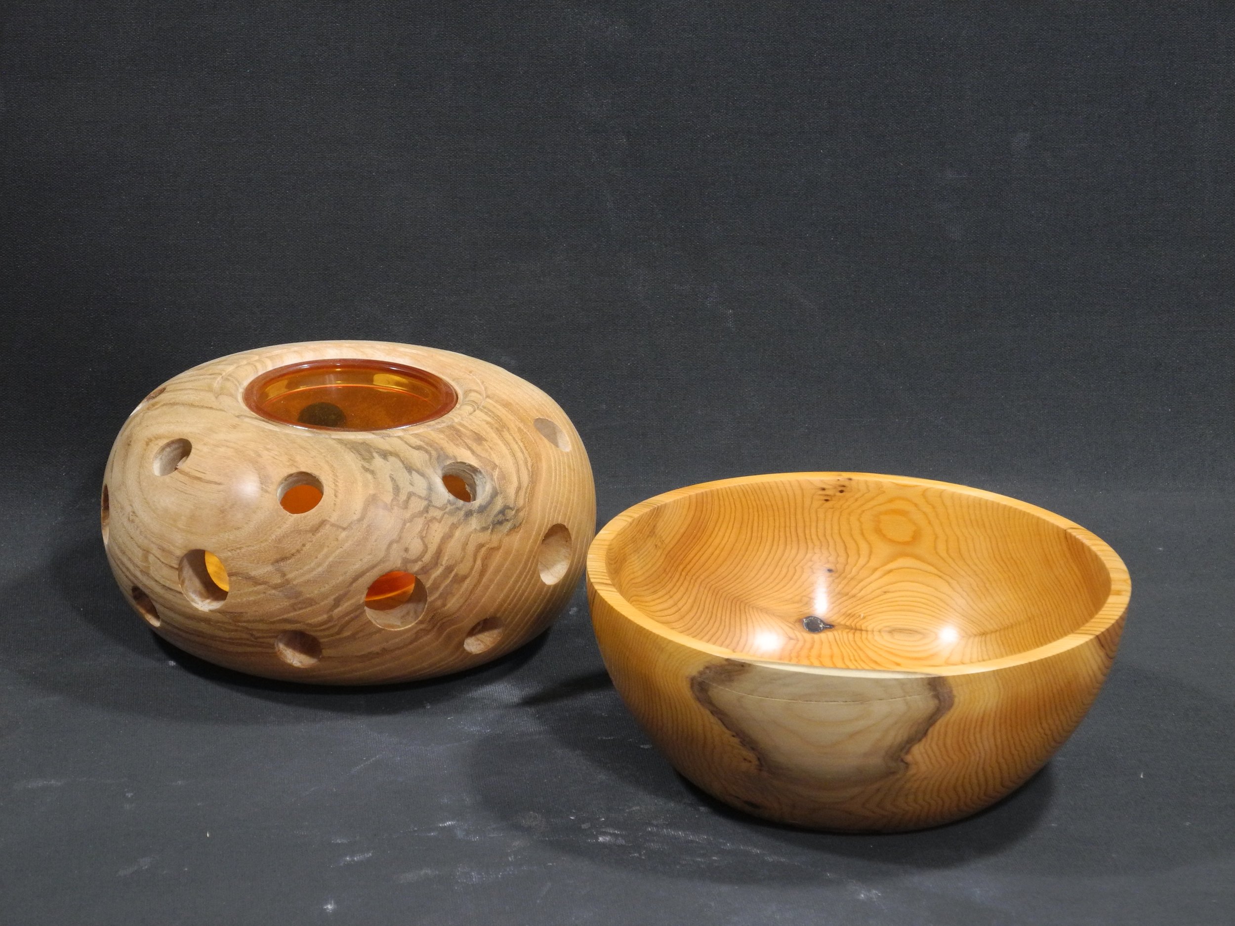 Wooden decorative bowl and a wooden bowl with a hollow design, both placed against a dark background.