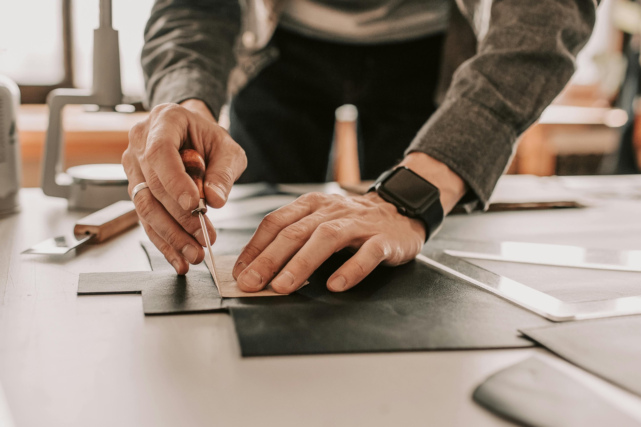A person using a hobby knife to cut a piece of leather on a worktable with various crafting tools.