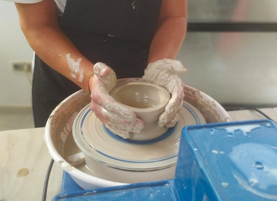 Person shaping a clay bowl on a pottery wheel with their hands covered in clay.