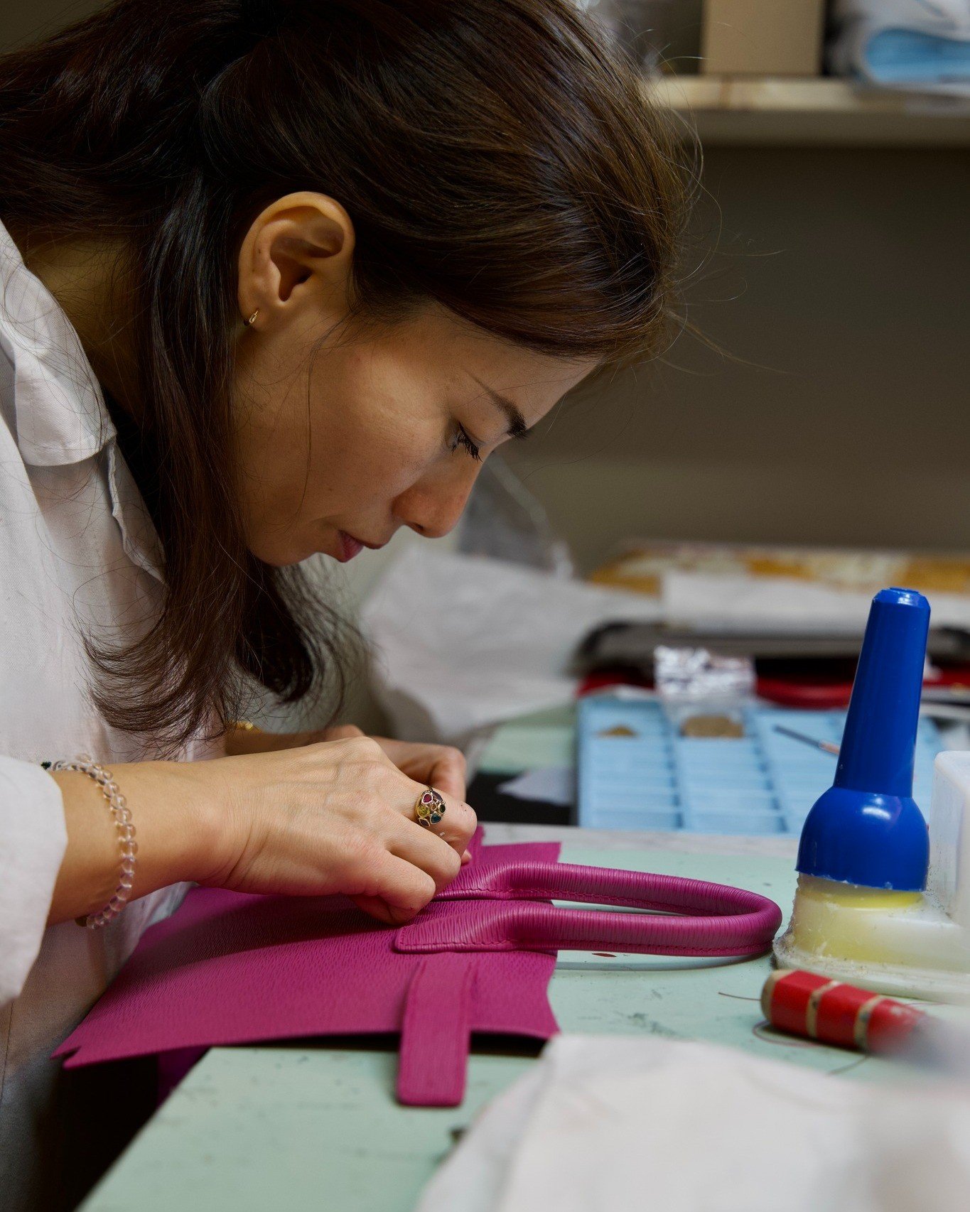 A woman working on a pink handbag at a work table, with various tools and supplies around her.