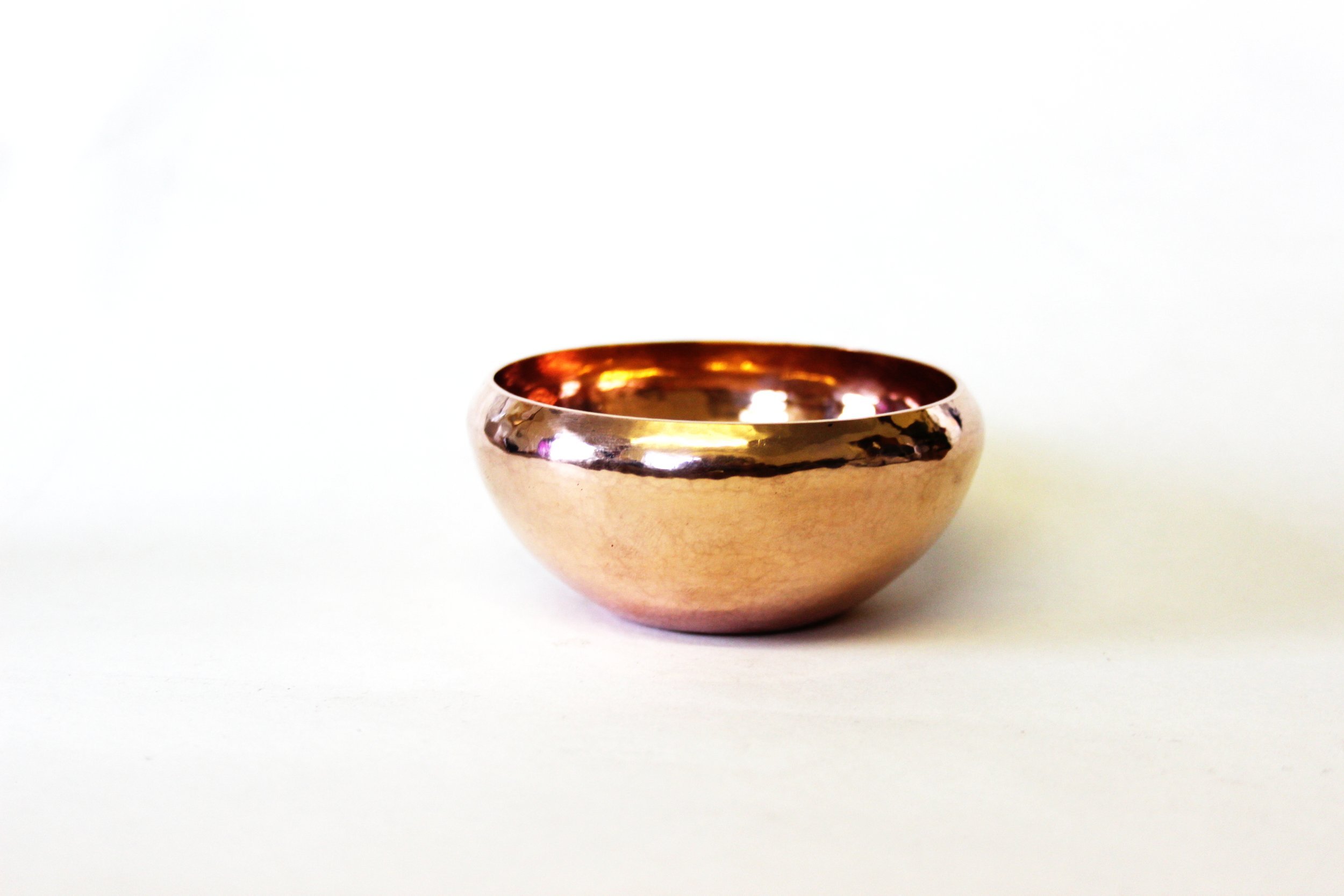 A shiny, metallic copper-colored bowl with a reflective surface placed on a plain white background.