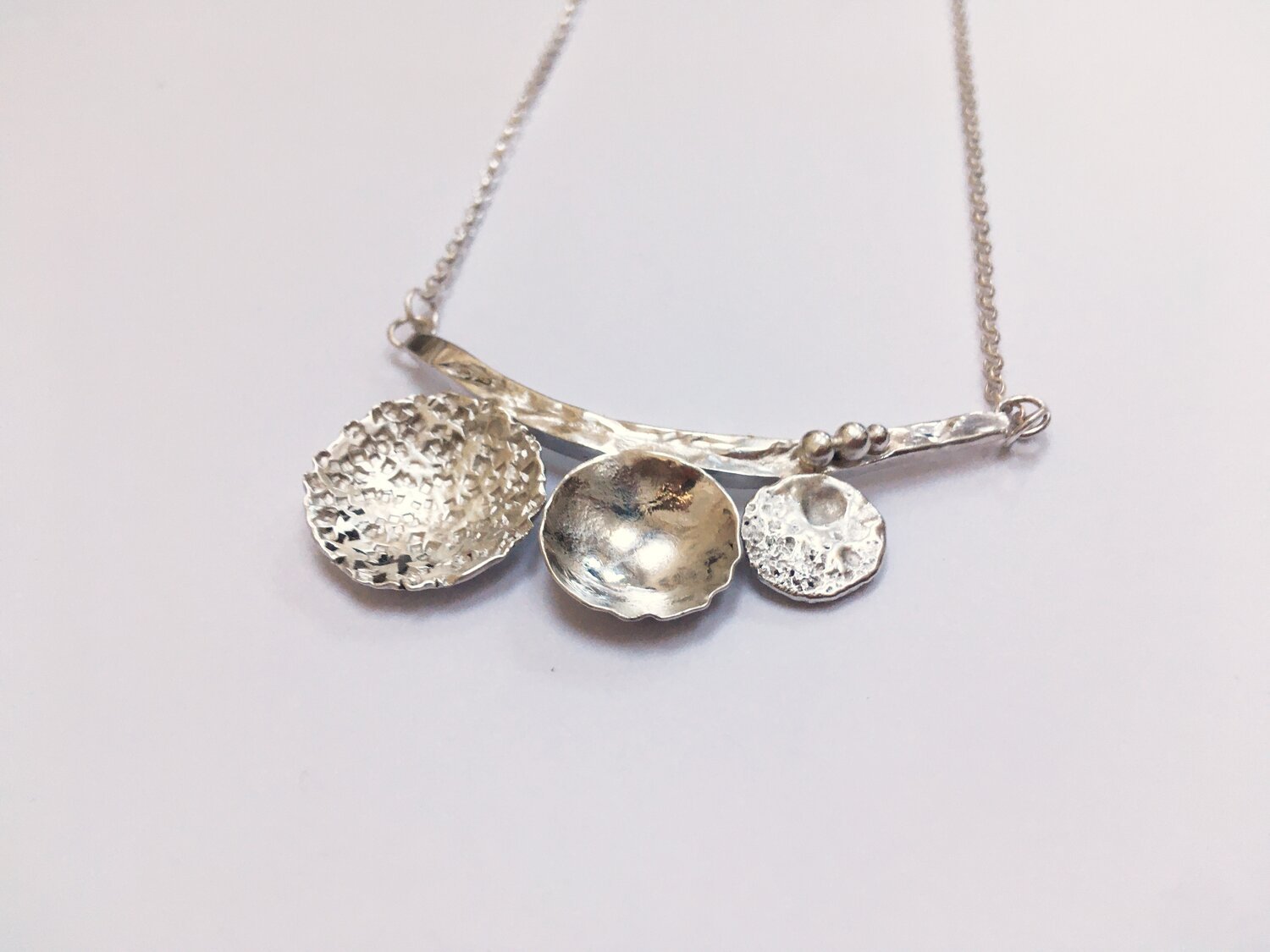 Handmade silver necklace with three textured, circular pendant charms on a white background.