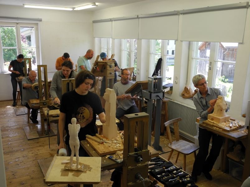 People working on wood sculptures in a woodworking studio with windows and various tools.