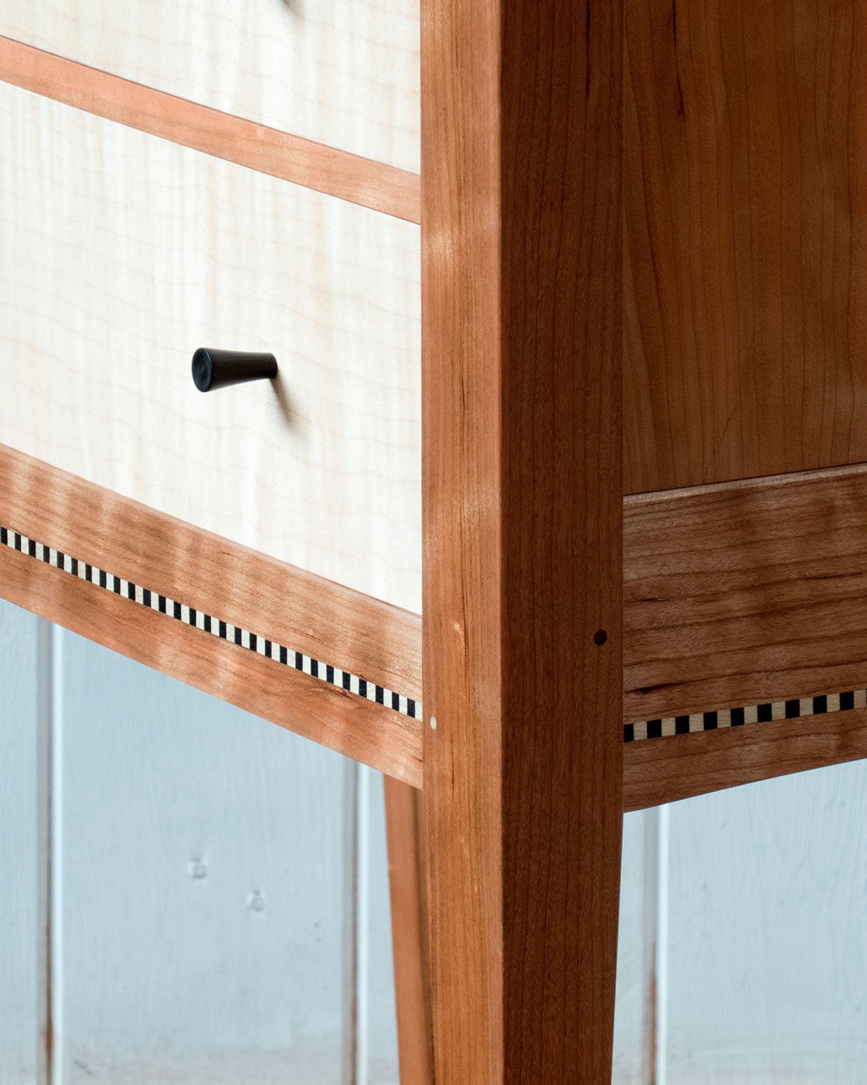 Close-up of a wooden drawer with a black knob and a decorative black and white striped border on a wooden cabinet
