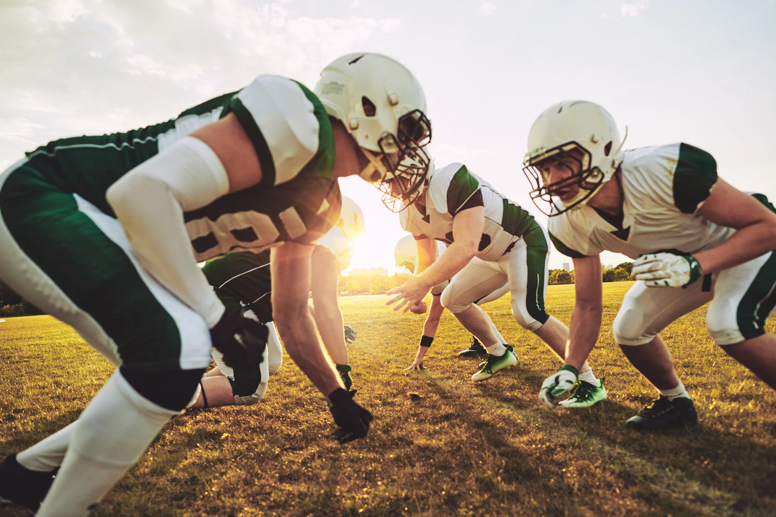 American football players in formation during a game at sunset.