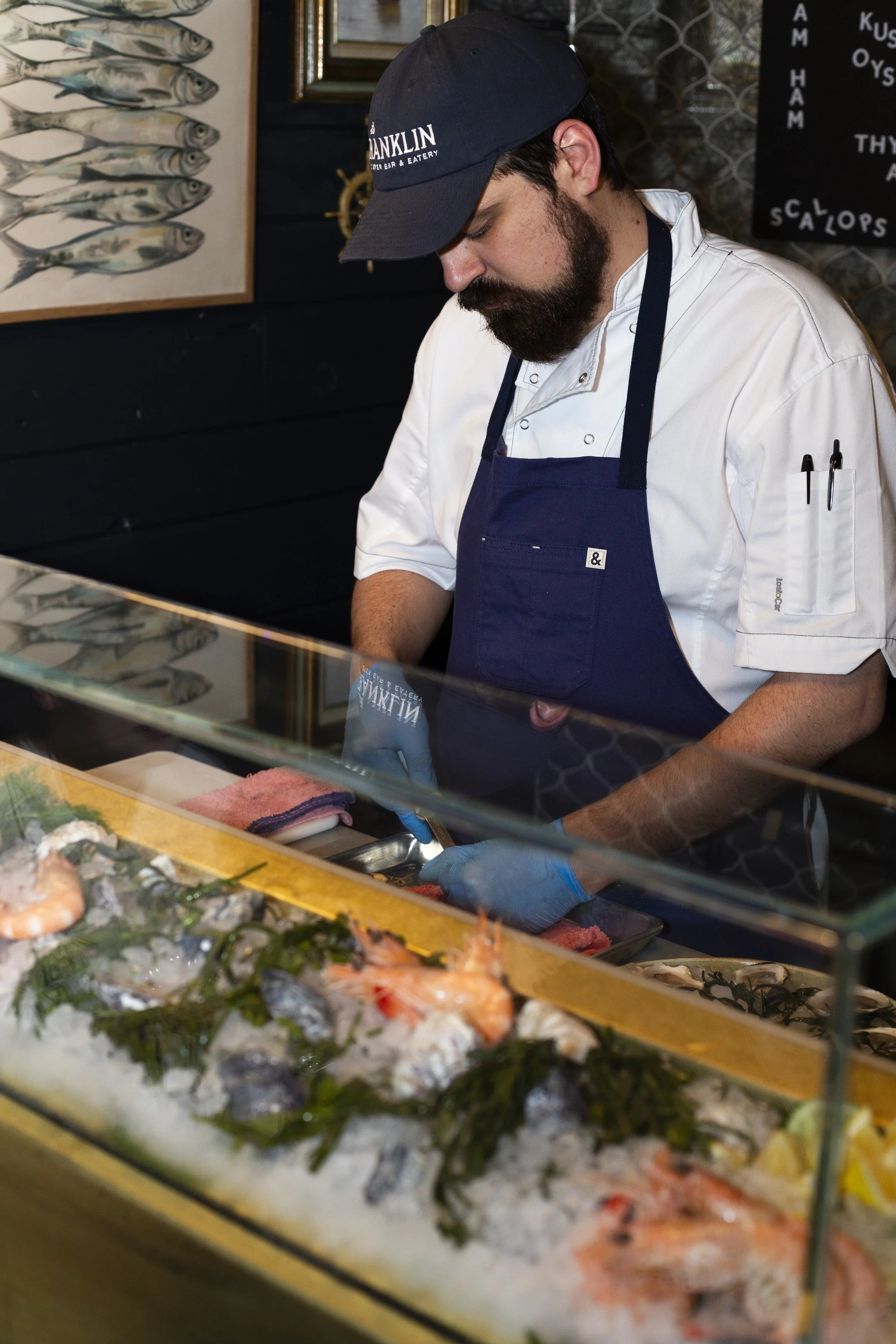 Chef preparing seafood behind glass display with ice and fresh shrimp.