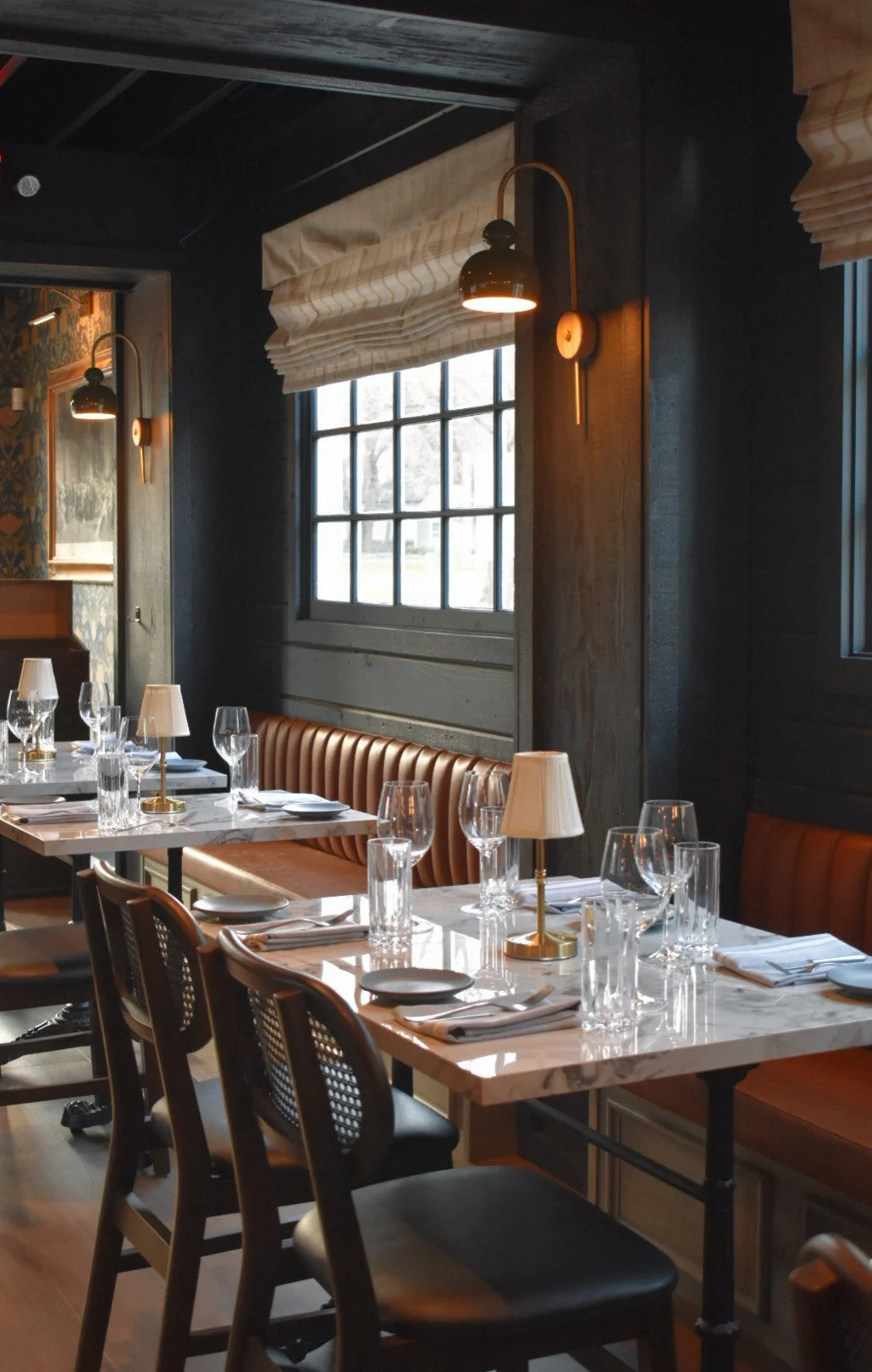 Interior of a restaurant with elegantly set tables, chairs, and wall sconces.