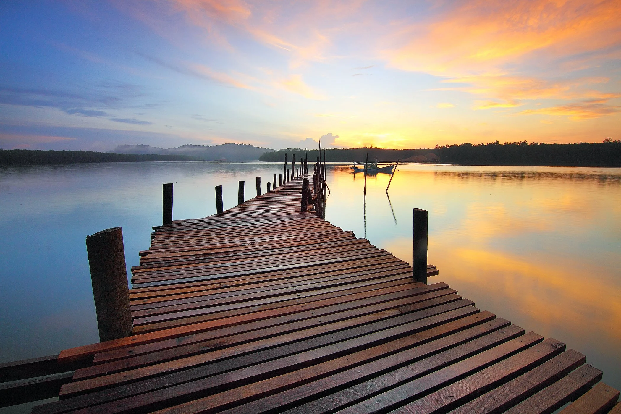 A wooden pier reaching out across calm water toward a golden sunrise
