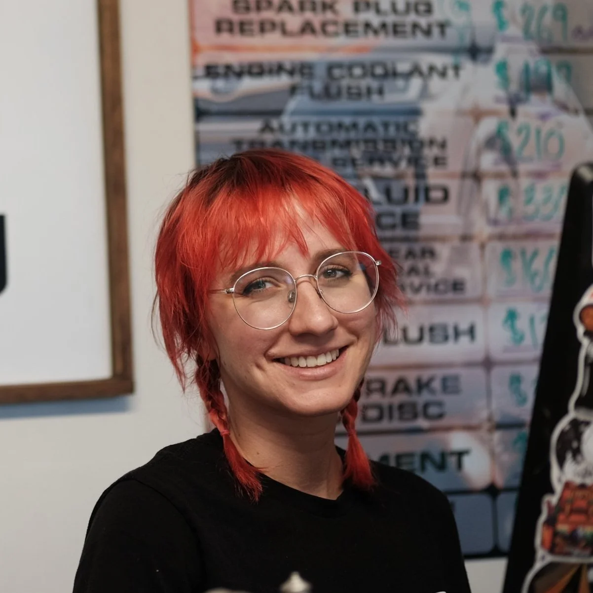 A woman with red hair and glasses smiles in the office, waiting to assist customers.