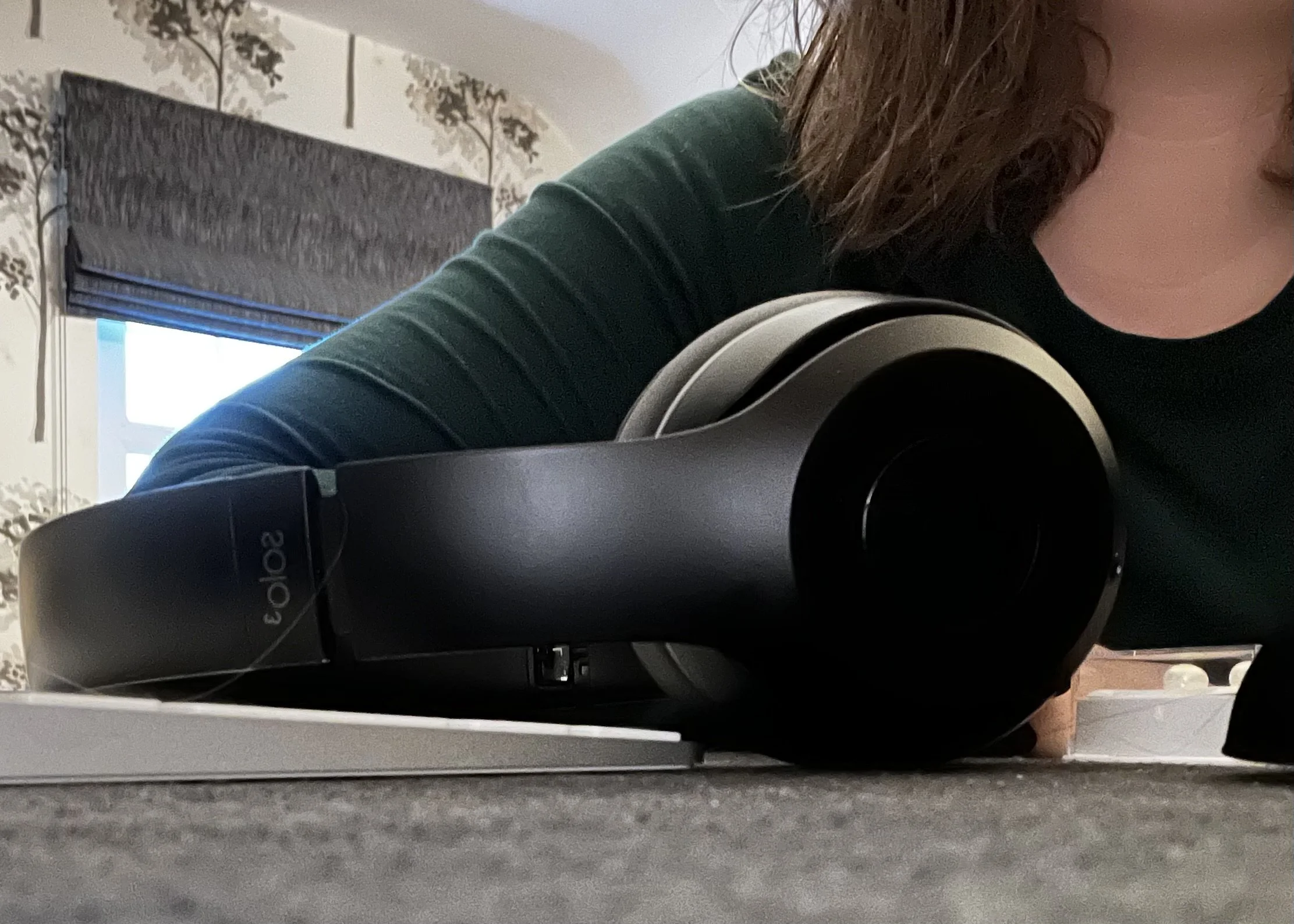 Close-up of a black and silver audio speaker on a table mat with a person's hair and part of their face visible in the background.