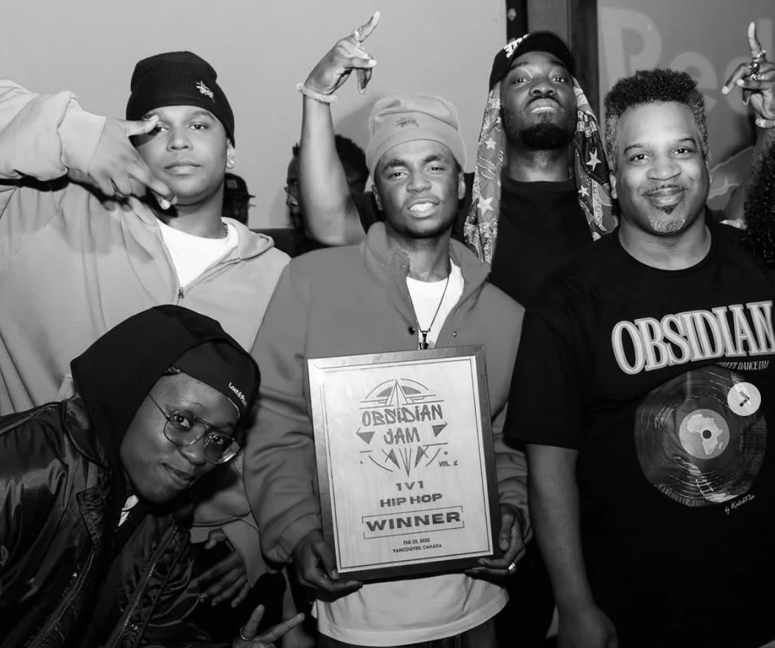 Group of five young men in casual clothing, one holding a framed certificate that reads 'Obsidian Jam Winner, Vancouver, Canada, 2018'. They are posing for the photo, some making peace signs or gang signs.