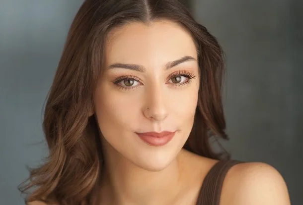 Close-up portrait of a smiling woman with short dark hair, wearing a peach-colored jacket and earrings.