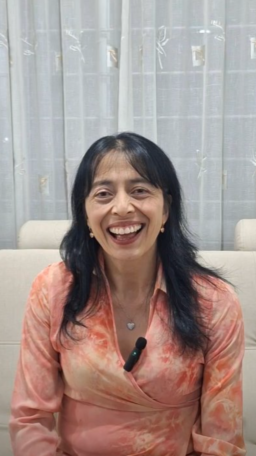 Mujer sonriente con un suéter color coral y un micrófono en un ambiente interior