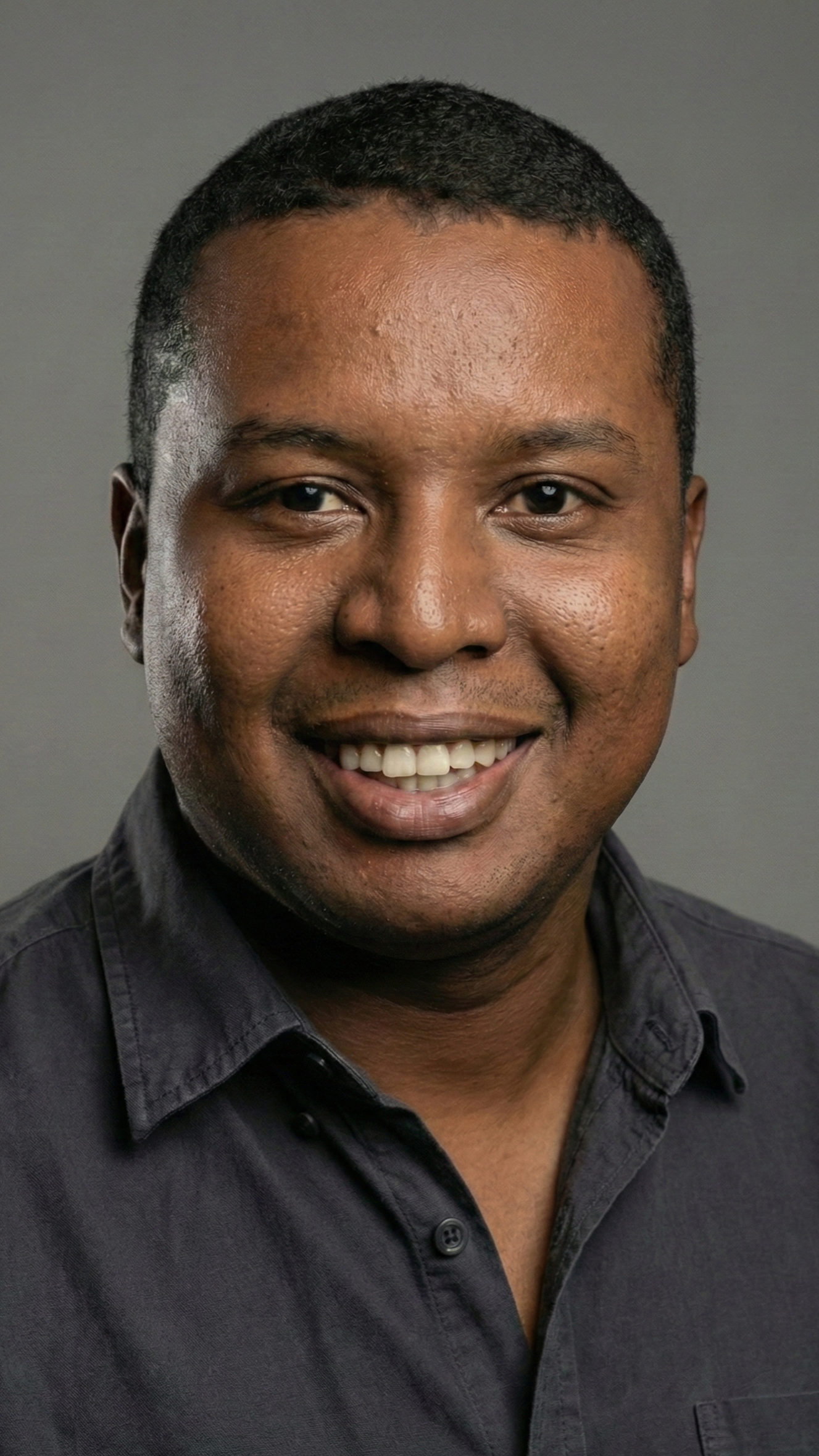 Retrato de un hombre con camisa negra, sonriendo. Fondo gris.