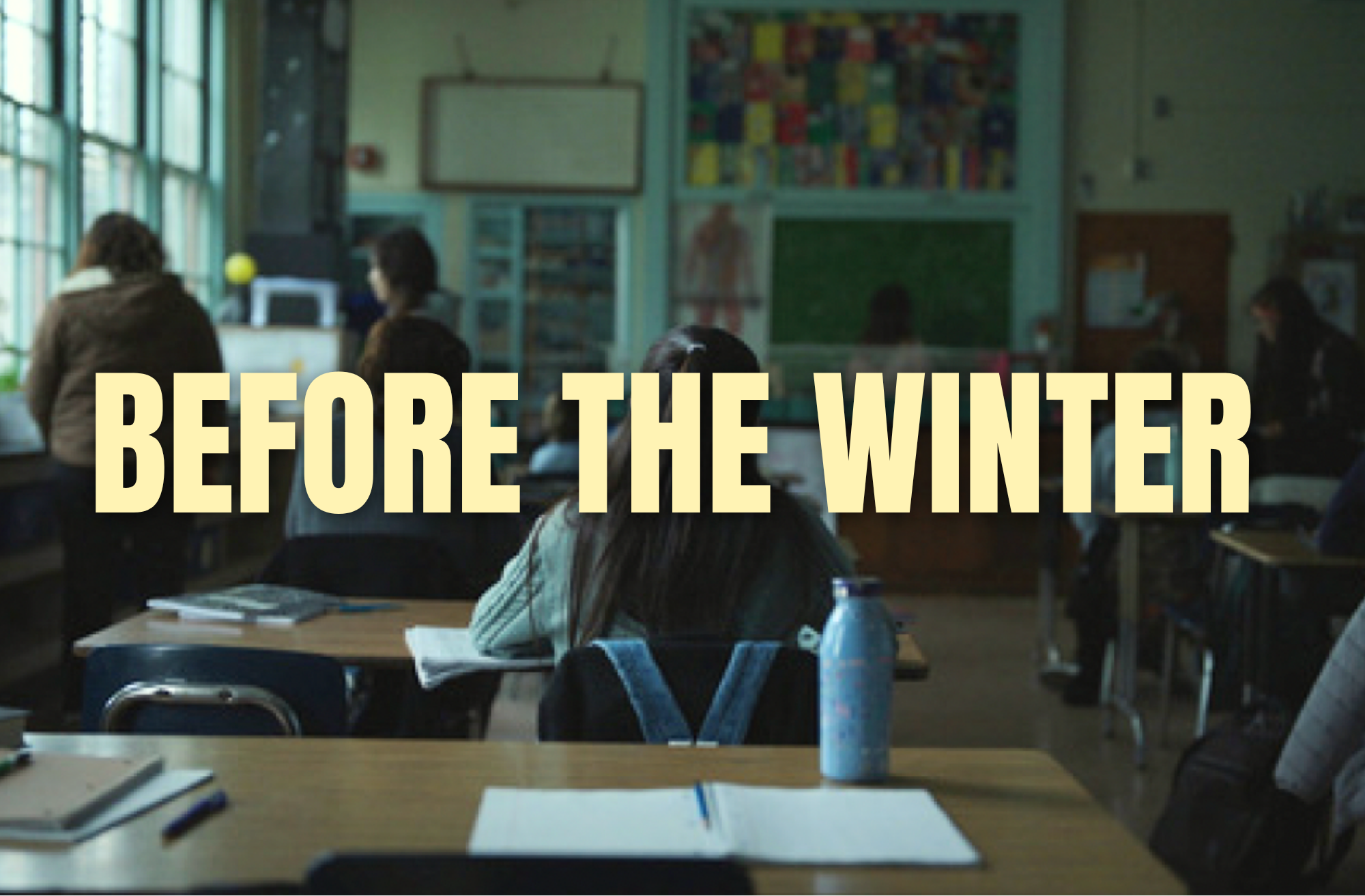 Classroom scene with students seated at desks, notebooks and water bottles in the foreground, a teacher at the front, educational posters, and windows with sunlight, overlaid with the text 'BEFORE THE WINTER'.
