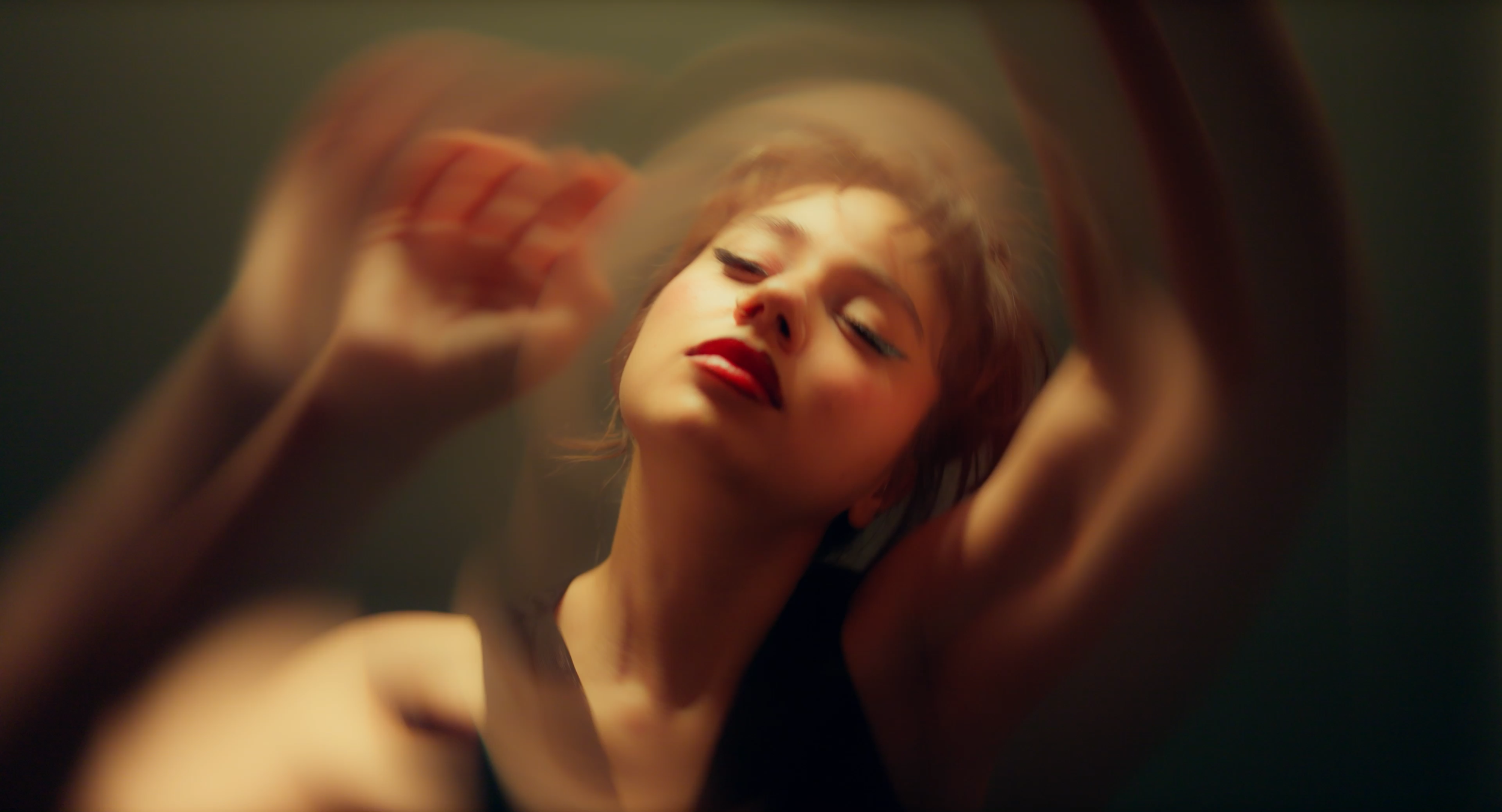 Music video still. BANA stands, lit by projector light.