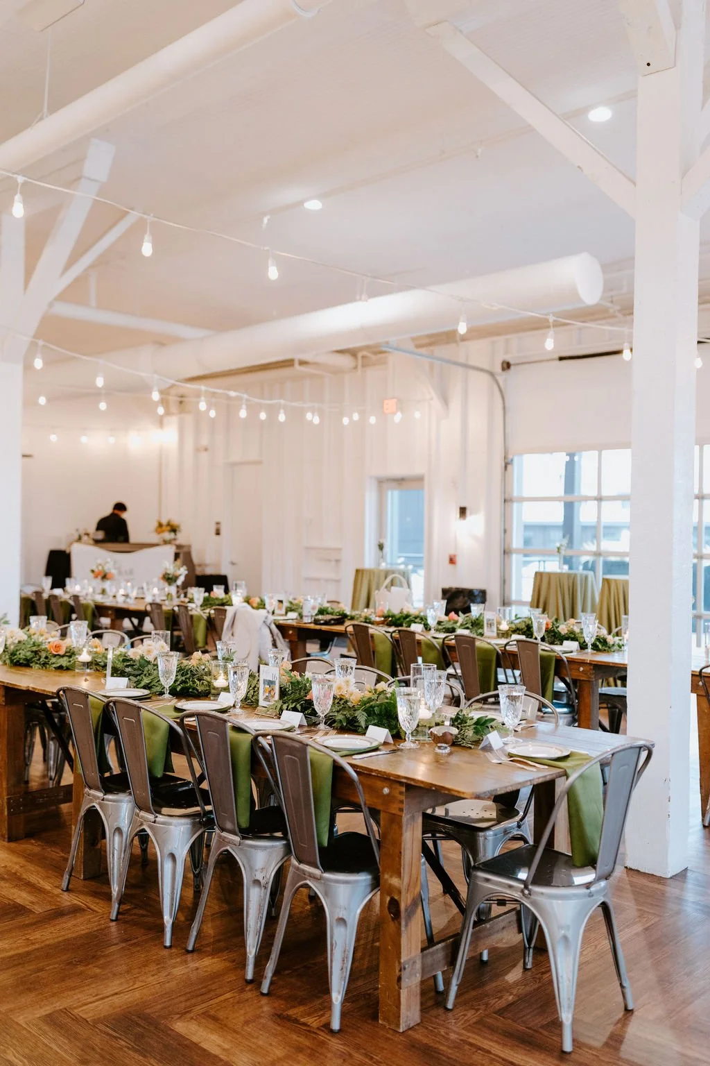 Table setting with white plates, gold utensils, a green table runner, a small framed photo, a gold name card that says 'Jackie', and glasses of water.