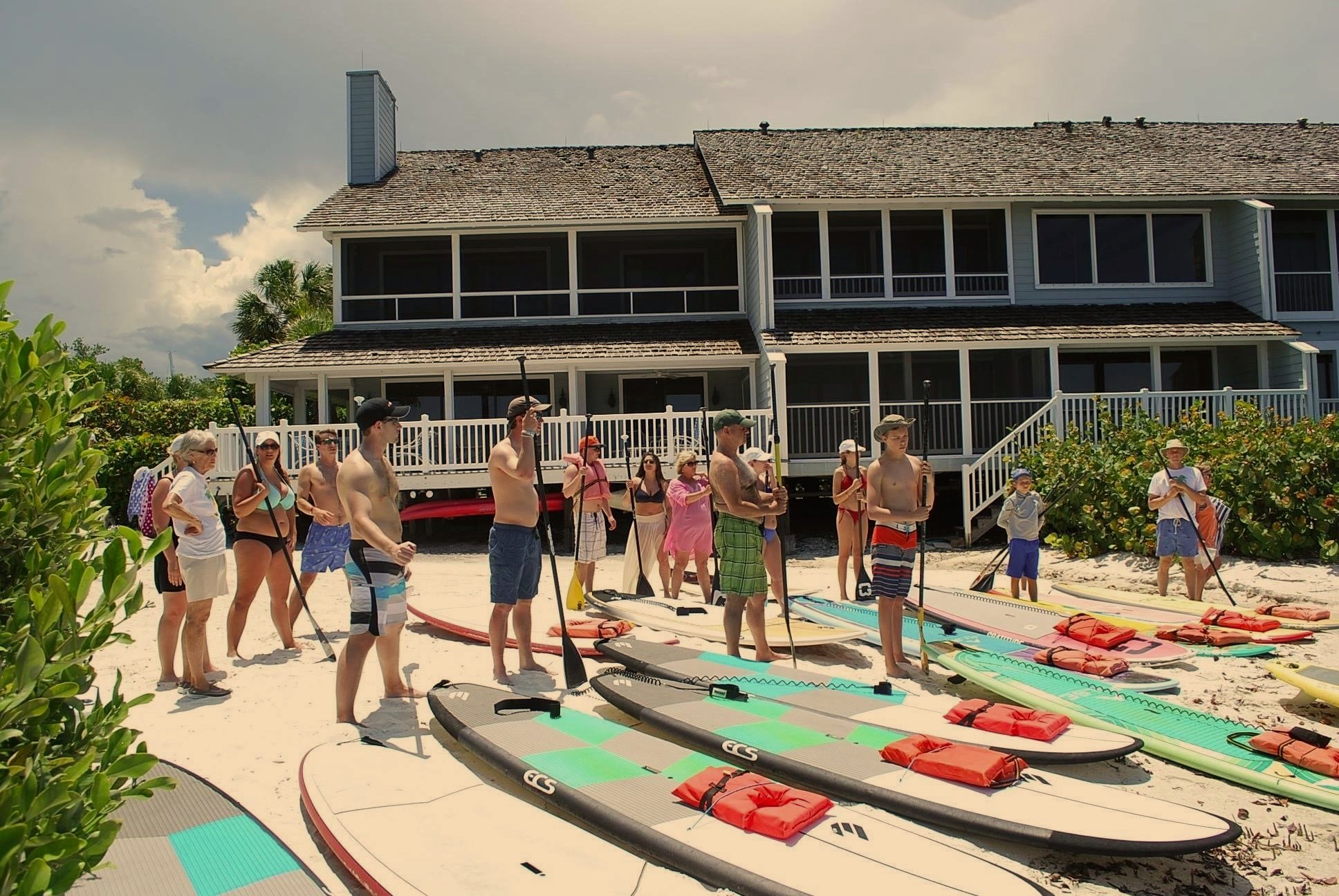 group of people standing in front of paddle boards listening to an instructor