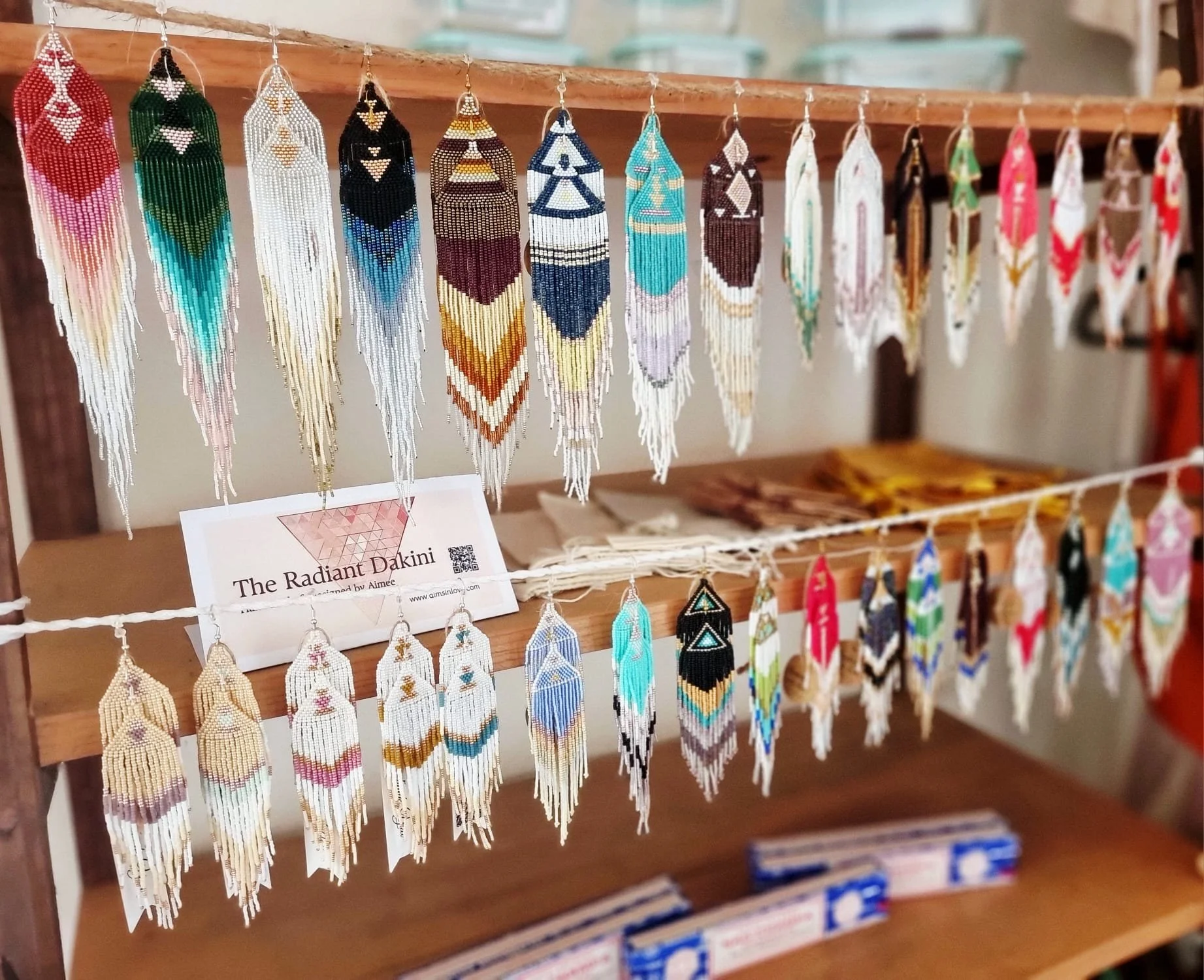 Colorful beaded feather earrings hanging on a wooden display rack at a yoga shop, with a variety of patterns and colors.