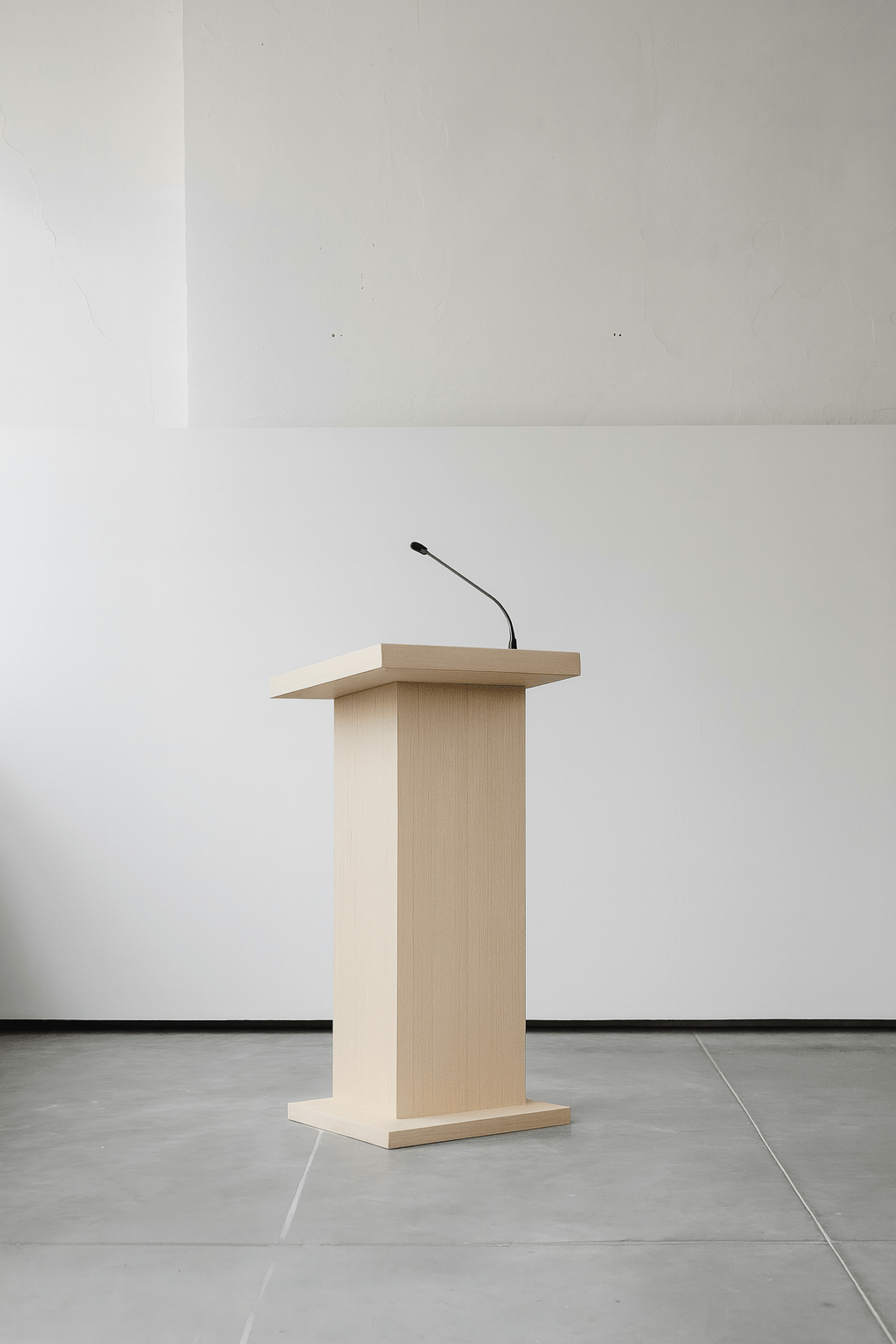 Empty wooden podium with a microphone in front of a plain white wall in a minimalist setting.