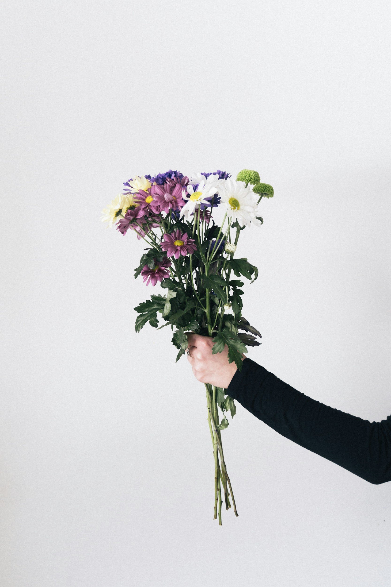 A person in a black long sleeve shirt is holding a bouquet of colorful flowers against a plain gray background.