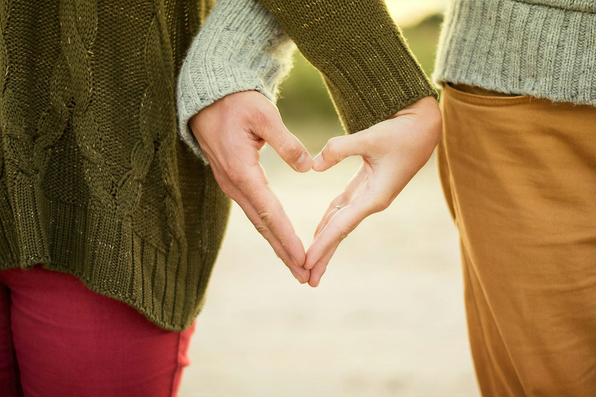 Two people forming a heart shape with their hands, wearing cozy sweaters.