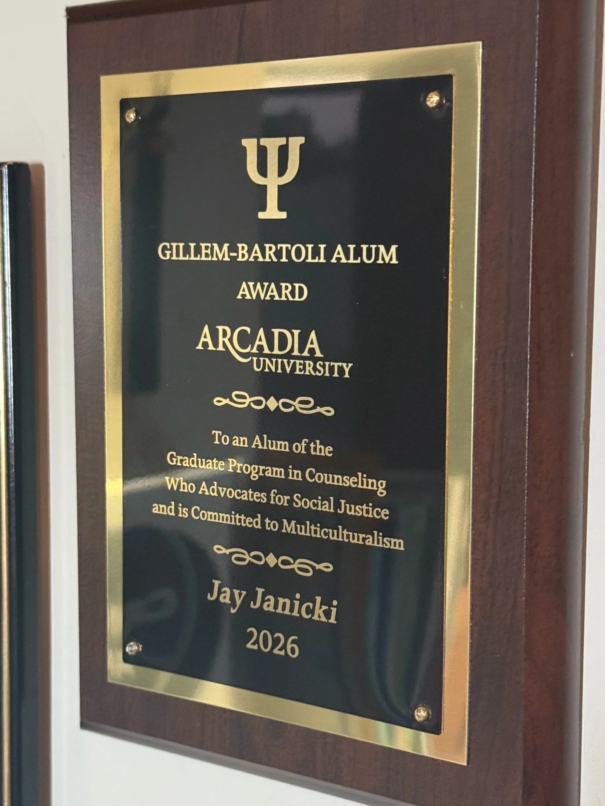 A plaque on a dark wooden background that honors Gillem-Bartoli Alum Award recipient Arcadia University, awarded to Jay Janicki, 2026.