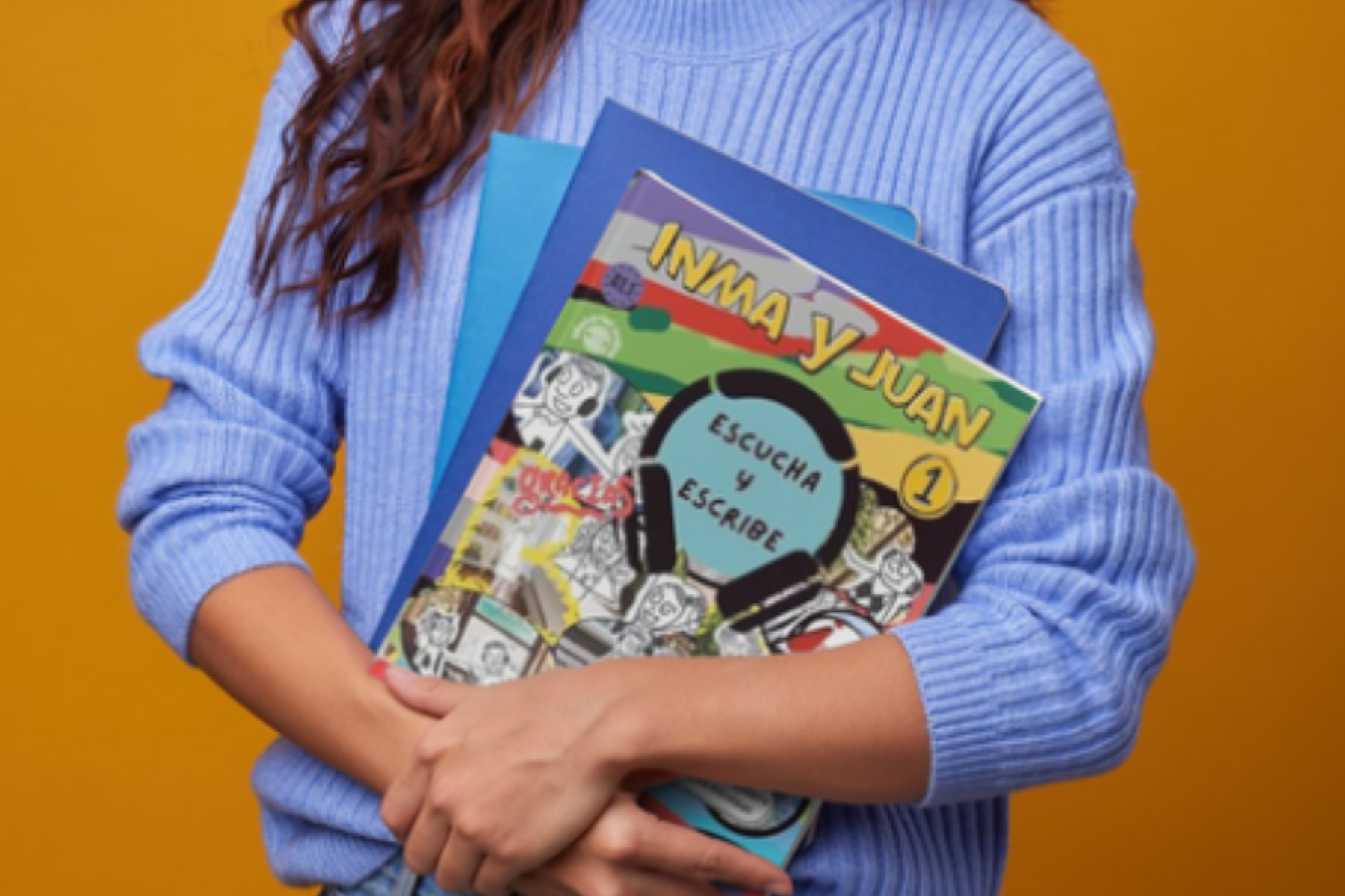 Person wearing a blue ribbed sweater holding colorful notebooks and a comic book against a yellow background.