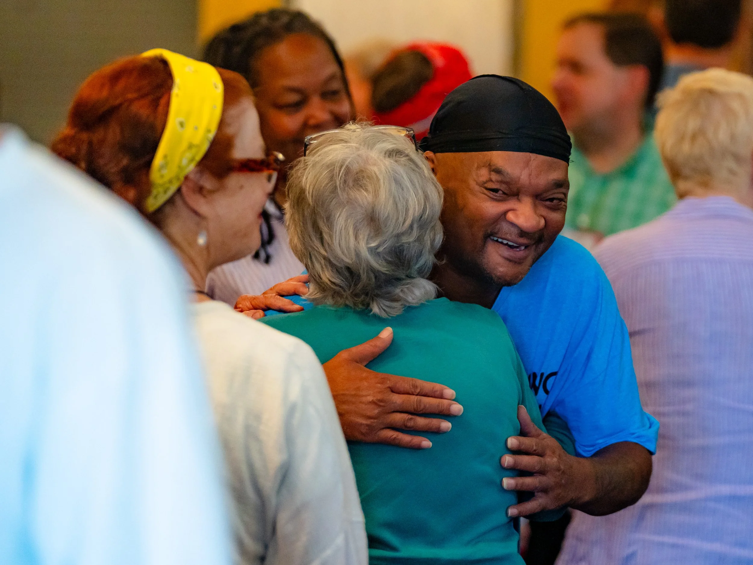 Group of diverse people hugging and smiling at an indoor event.