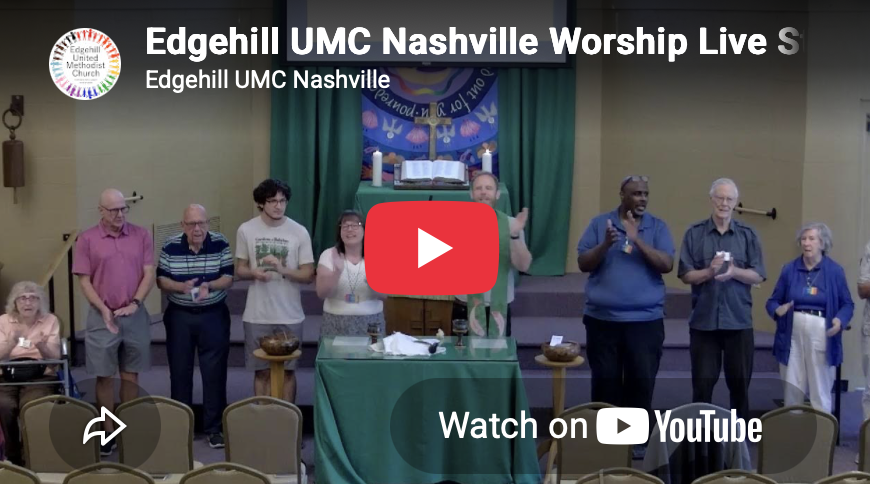 A group of people standing on a church stage, with some holding candles and others with their hands raised, during a worship service at Edgehill UMC Nashville. A table with a green cloth and an open book is in the foreground. The background features a cross, candles, and a religious banner.