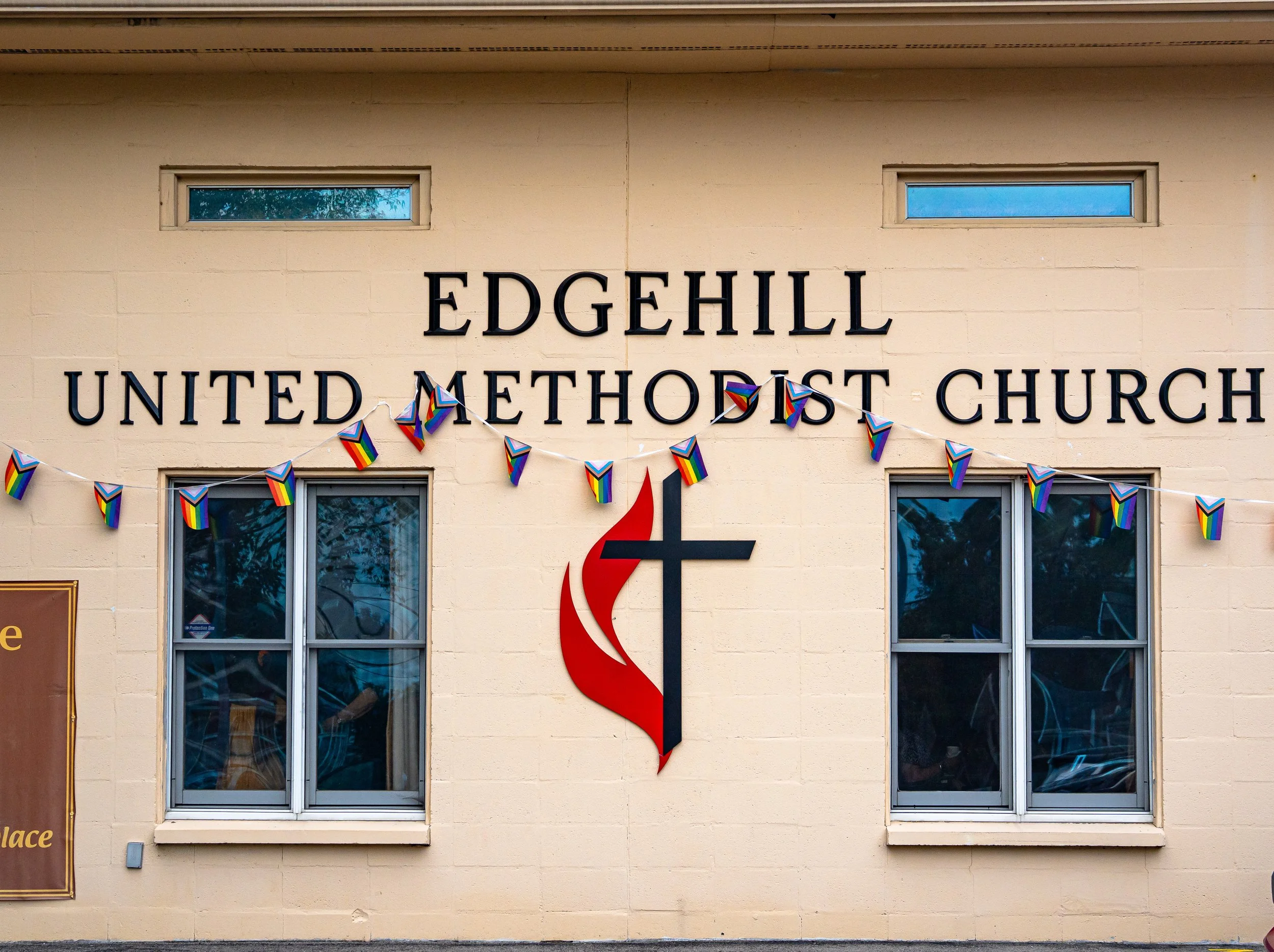 Exterior of Edgehill United Methodist Church with rainbow pride flags hanging across windows and a red flame symbol.