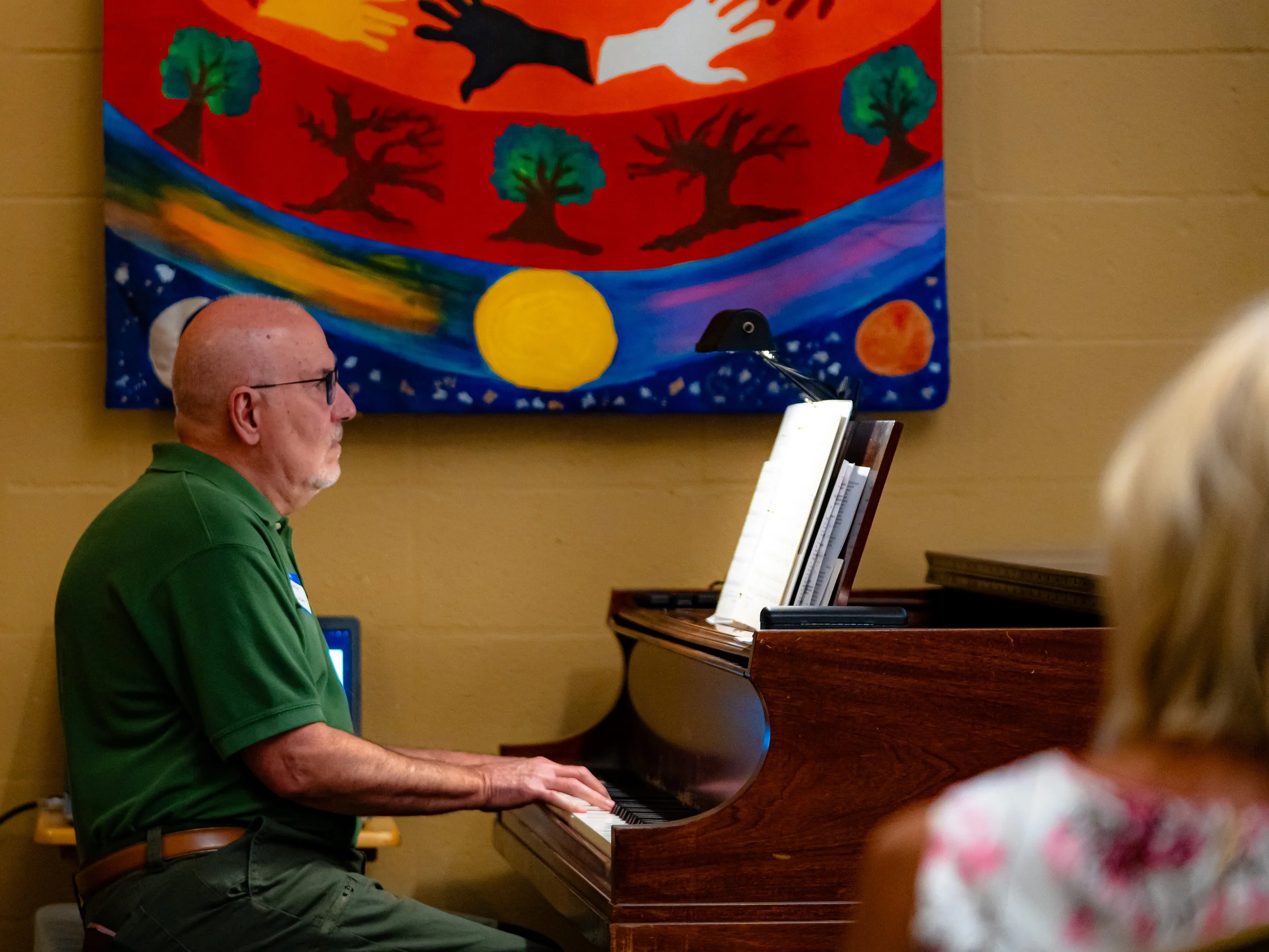 An elderly man with glasses and a green shirt playing a piano.