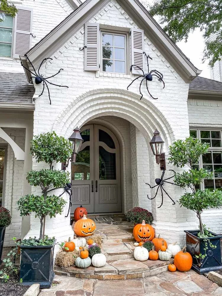 Decorated house with Halloween pumpkins, spider decorations, and potted plants at the entrance.