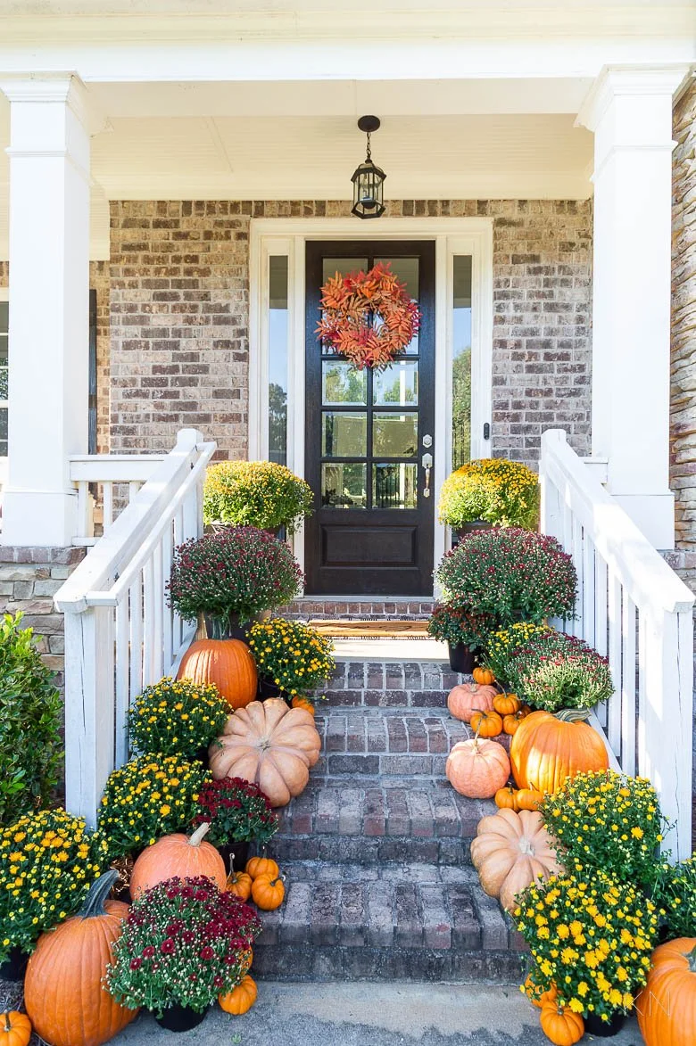 Fall decorated front porch with pumpkins, chrysanthemums, and a fall wreath