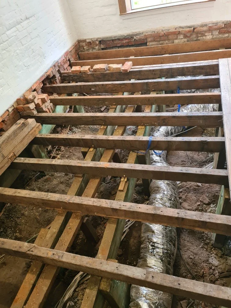 Room with exposed wooden floor joists and ventilation ductwork, indicating ongoing renovation or construction.