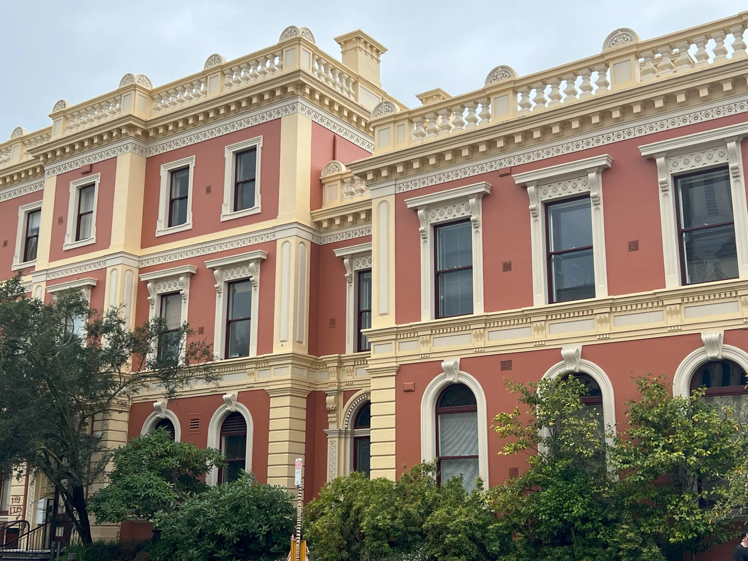 A historic pink and cream colored building with ornate white trim, multiple windows, and decorative rooftop railing.