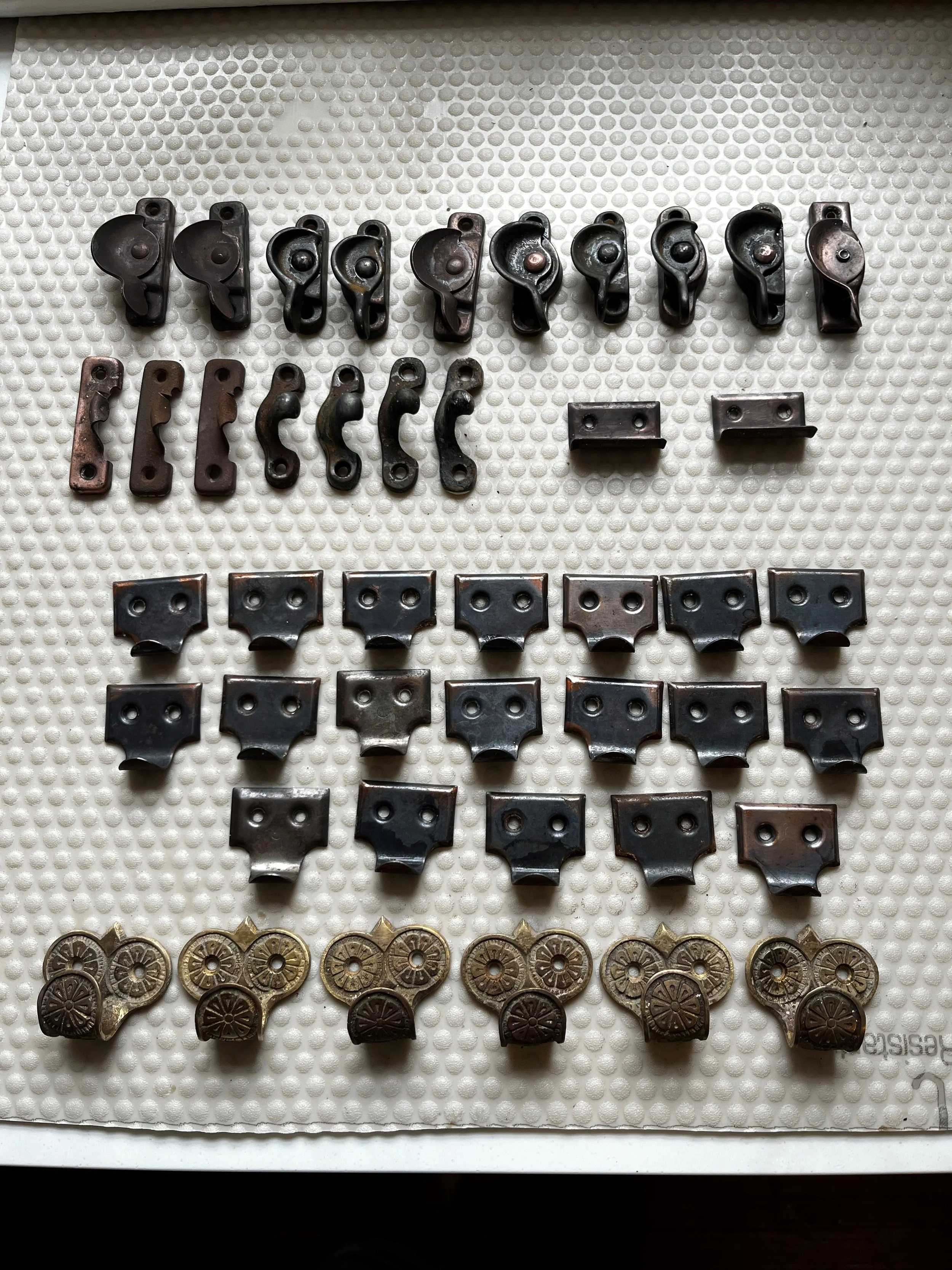 Collection of vintage door roller and hinge hardware parts arranged on a textured white surface.