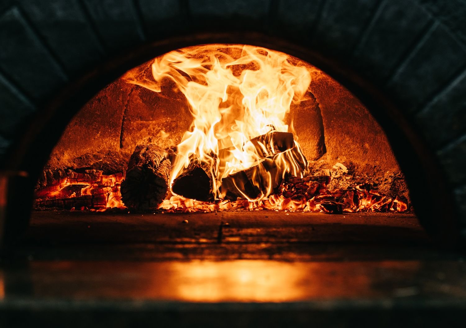Close-up of burning logs in a wood-fired oven with flames rising inside.