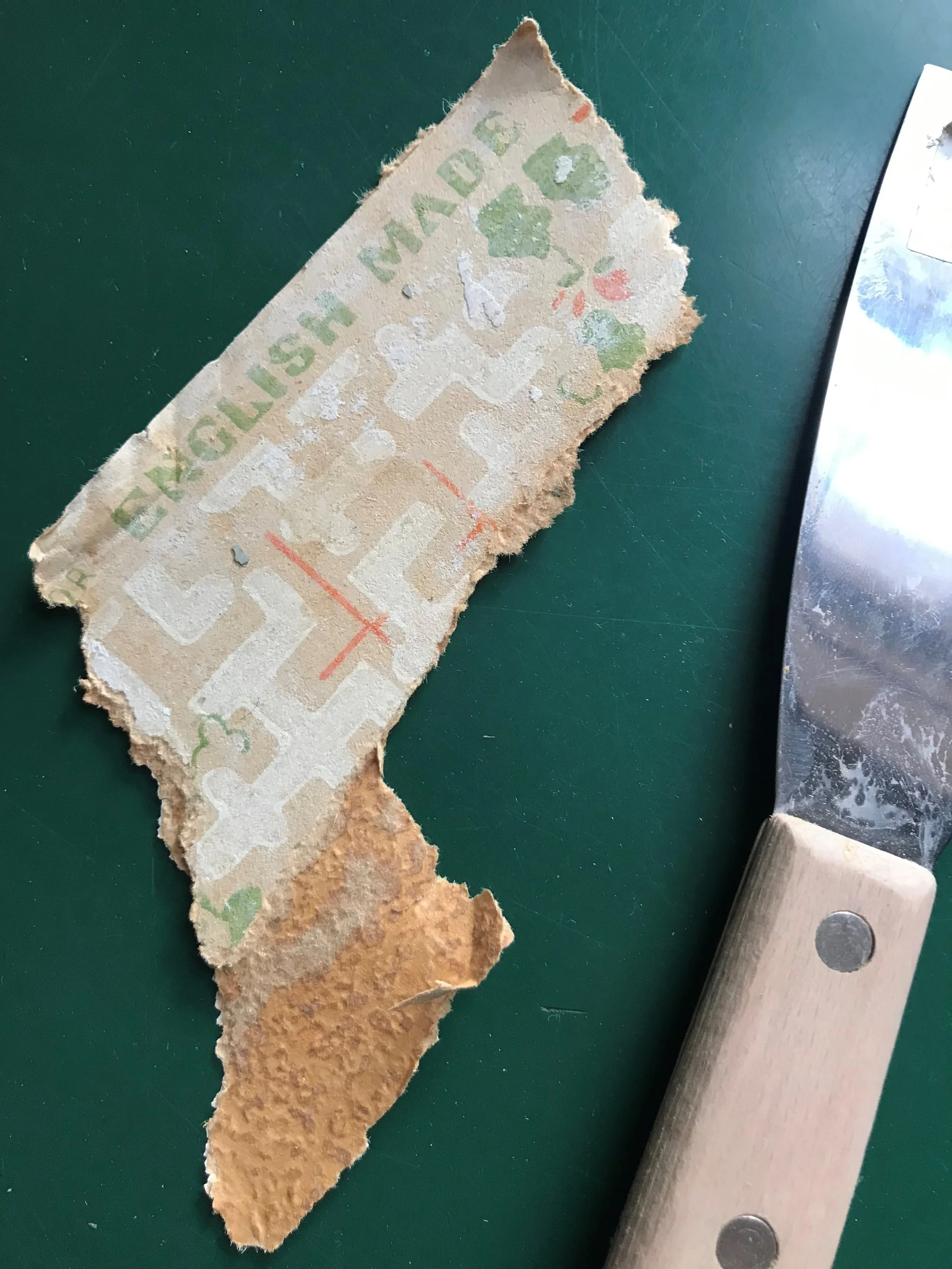 A torn piece of paper or fabric with the words 'ENGLISH MADE' and a partial map or design, placed on a green surface next to a large metal spatula with a wooden handle.