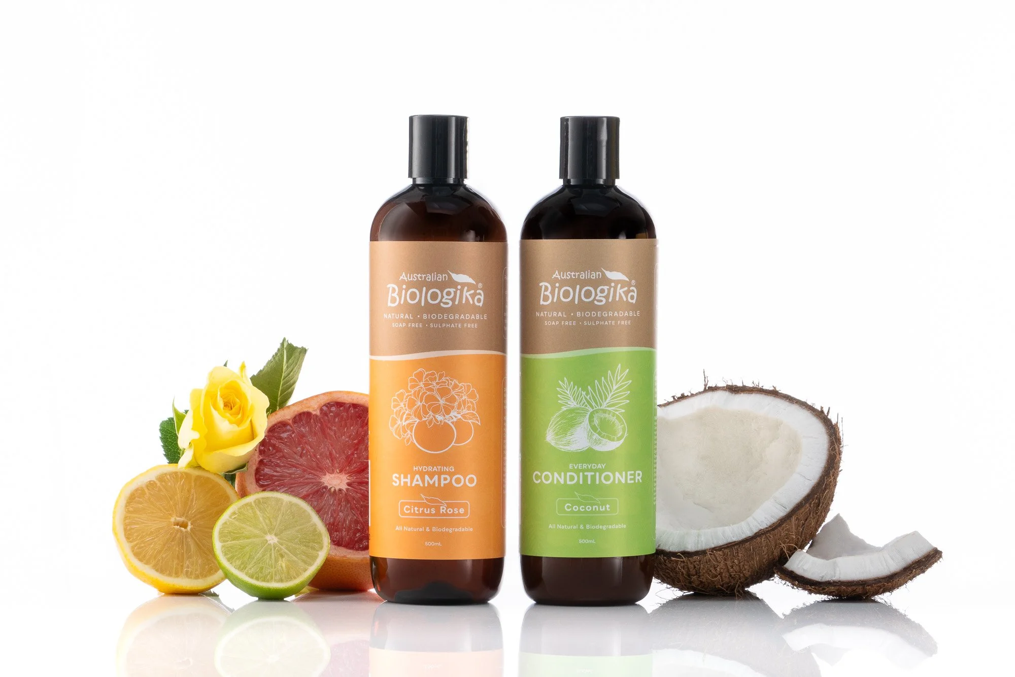 Two bottles of Australian Biologika shampoo and conditioner surrounded by fruits and coconut pieces on a white background.