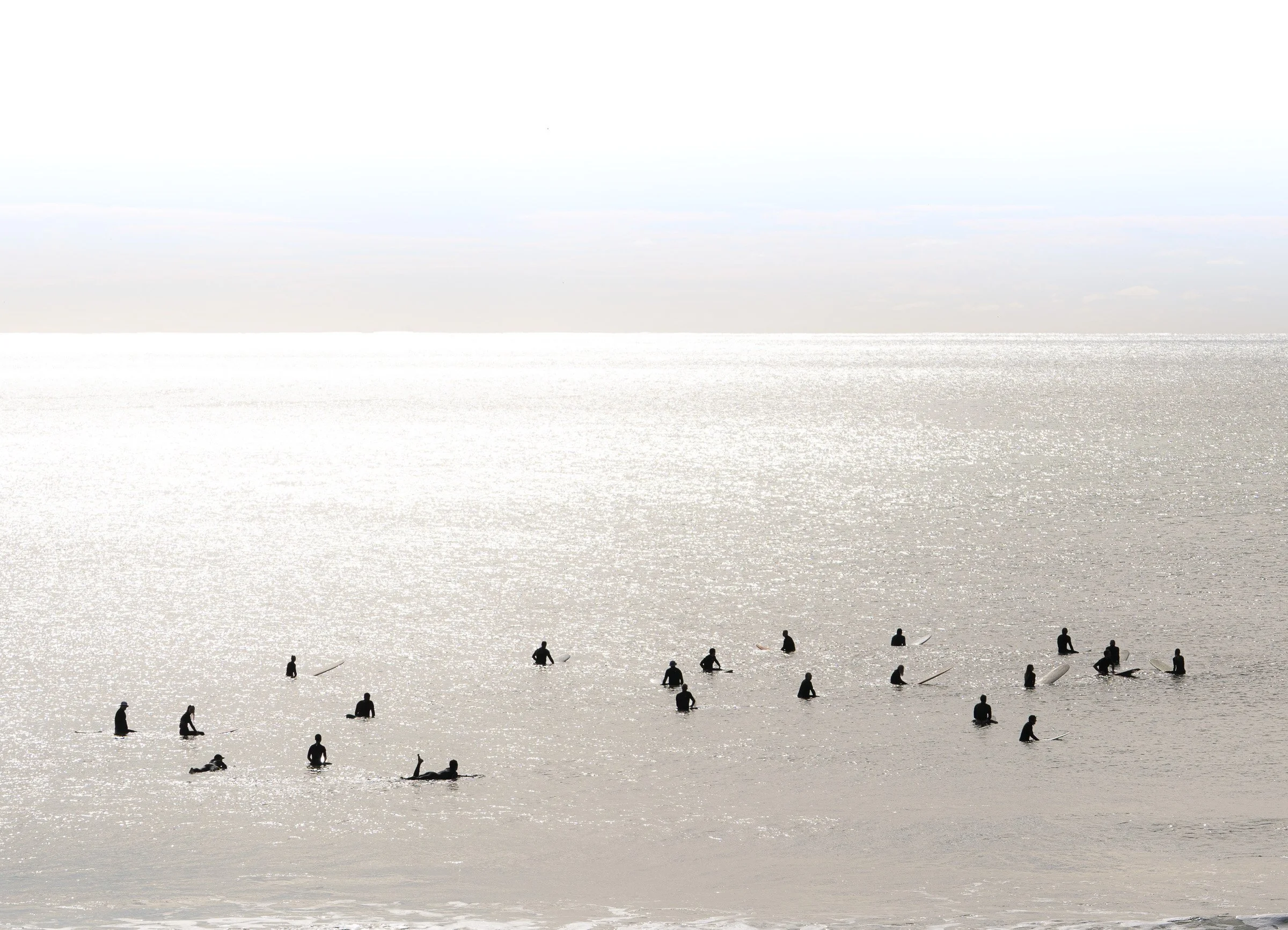 People surfing and standing in the water at the beach during sunset or sunrise.