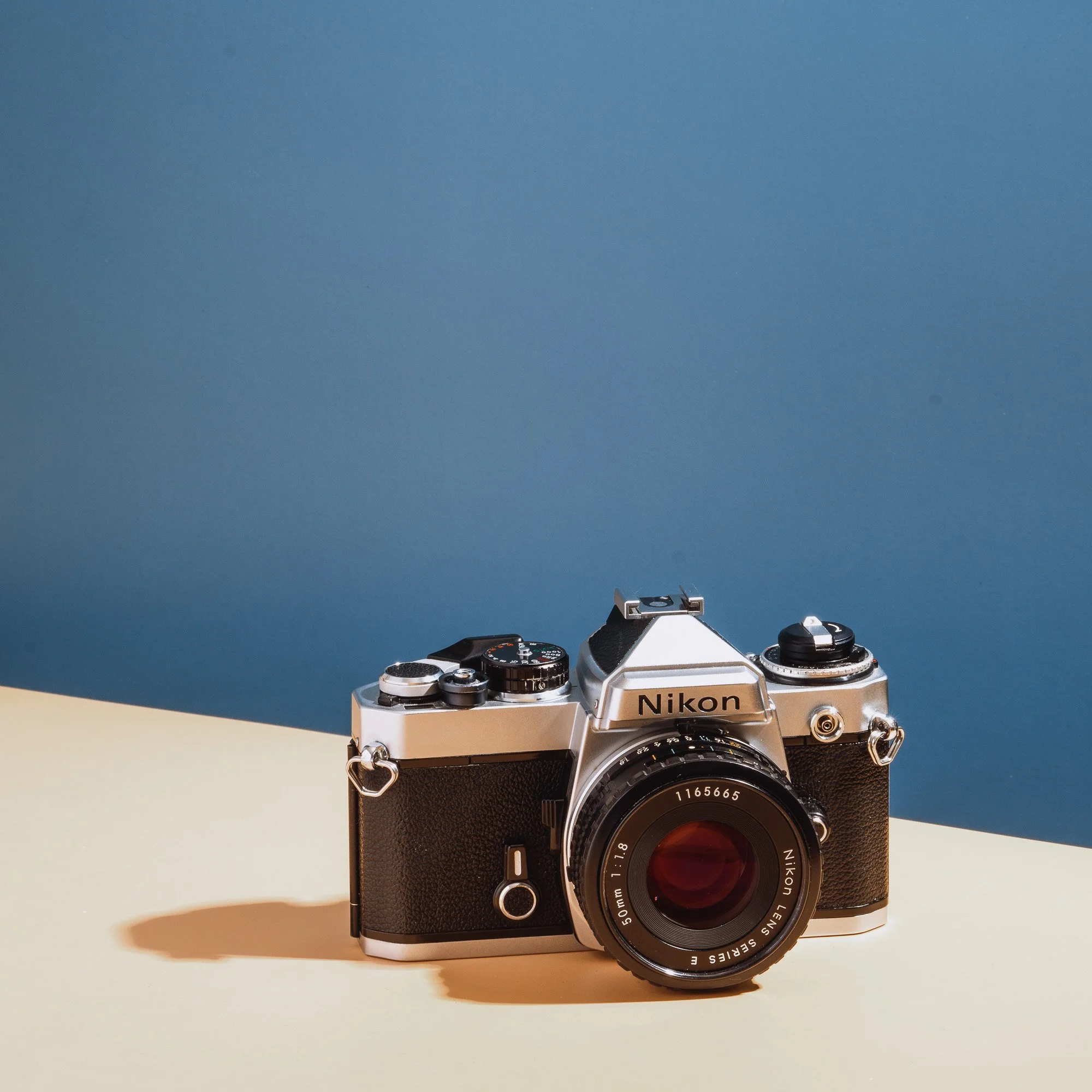 A vintage Nikon camera with a wide lens atop a beige surface, against a gradient blue background.
